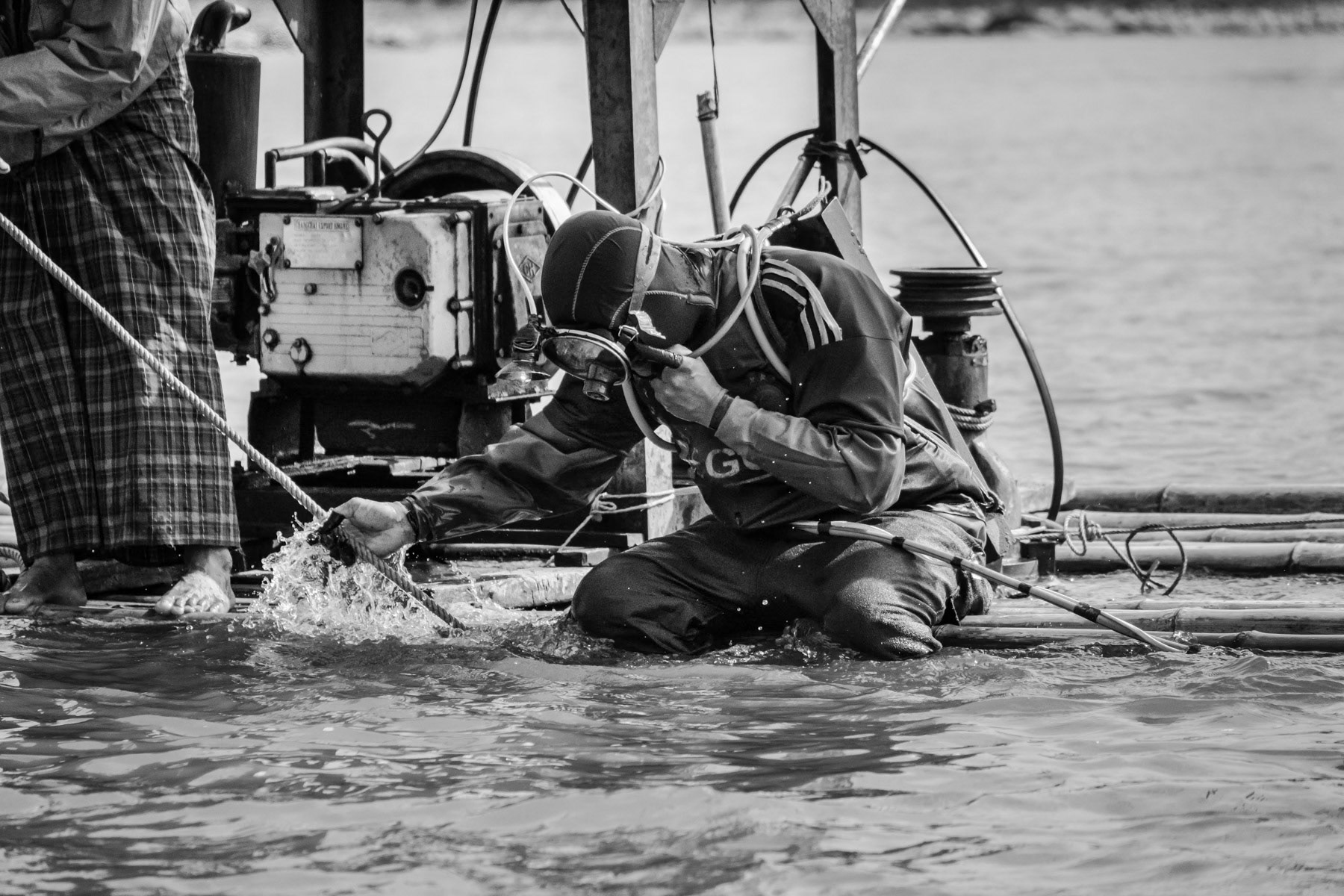 A gold diver fixing his compressed air supply and head lamp before diving to the riverbed where he will stay 3-4 hours and collect river soil through a sucking hose. Gold will afterwards be extracted from the soil using extremely toxic mercury. Irrawaddy River, Myitkyina Township, Kachin State, Myanmar, February 2020