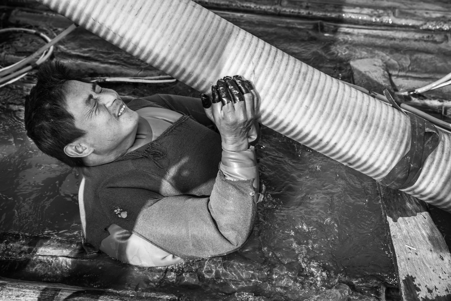A gold diver getting ready to spend 3-4 hours underwater sucking up soil and sediment from the riverbed through the large hose. A team of 2 divers make in average 60 to 80 USD per day during the gold diving season between December and March. Irrawaddy River, Kachin State, Myanmar, February 2020