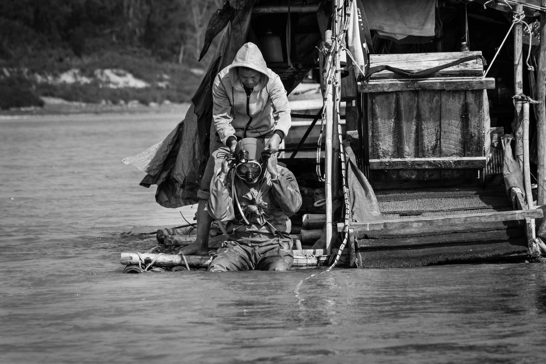 A gold diver fixing his compressed air supply and head lamp before diving to the riverbed where he will stay 3-4 hours and collect river soil through a sucking hose. Gold will afterwards be extracted from the soil using extremely toxic mercury. Irrawaddy River, Myitkyina Township, Kachin State, Myanmar, February 2020