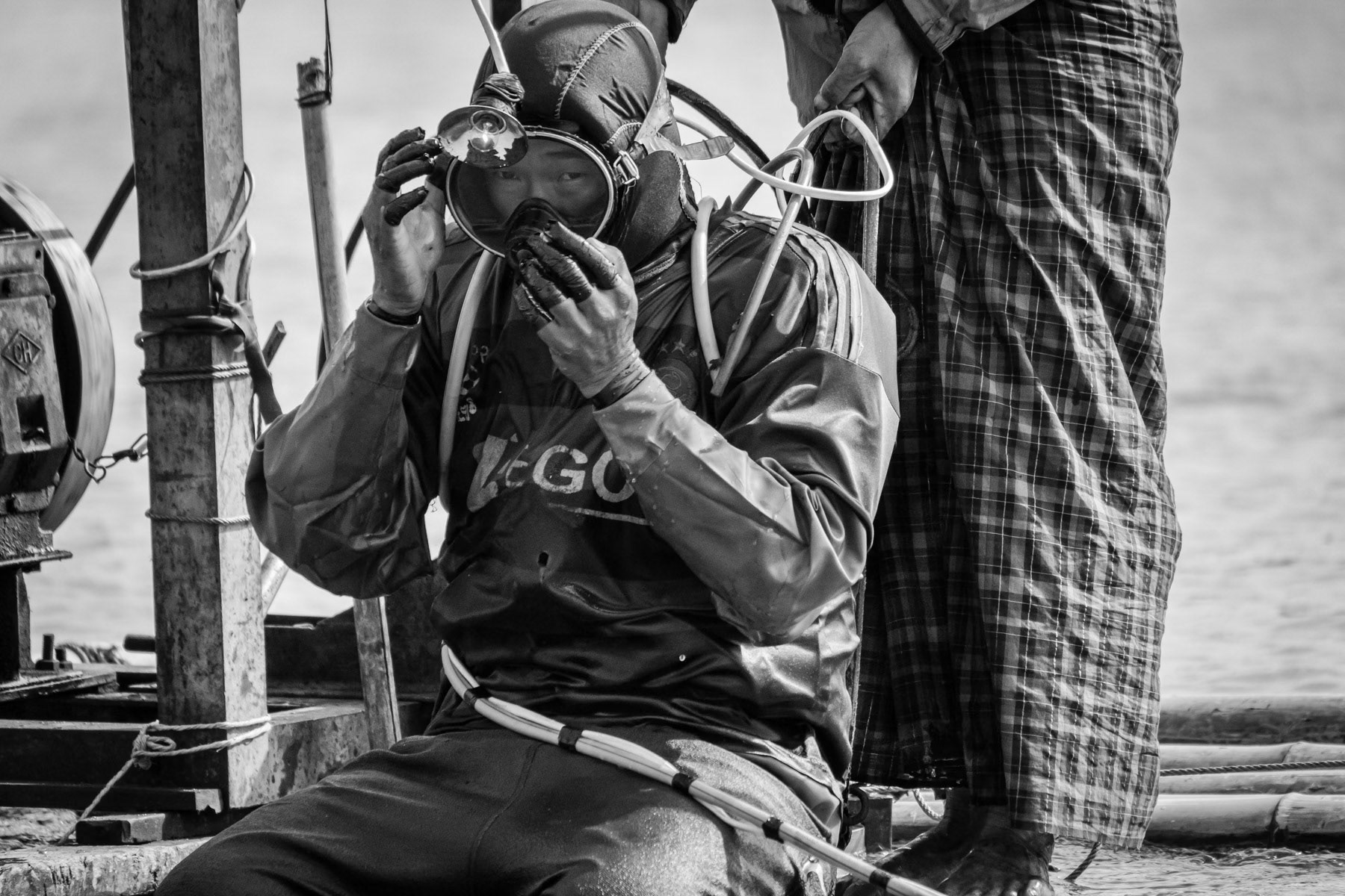A gold diver fixing his compressed air supply and head lamp before diving to the riverbed where he will stay 3-4 hours and collect river soil through a sucking hose. Gold will afterwards be extracted from the soil using extremely toxic mercury. Irrawaddy River, Myitkyina Township, Kachin State, Myanmar, February 2020