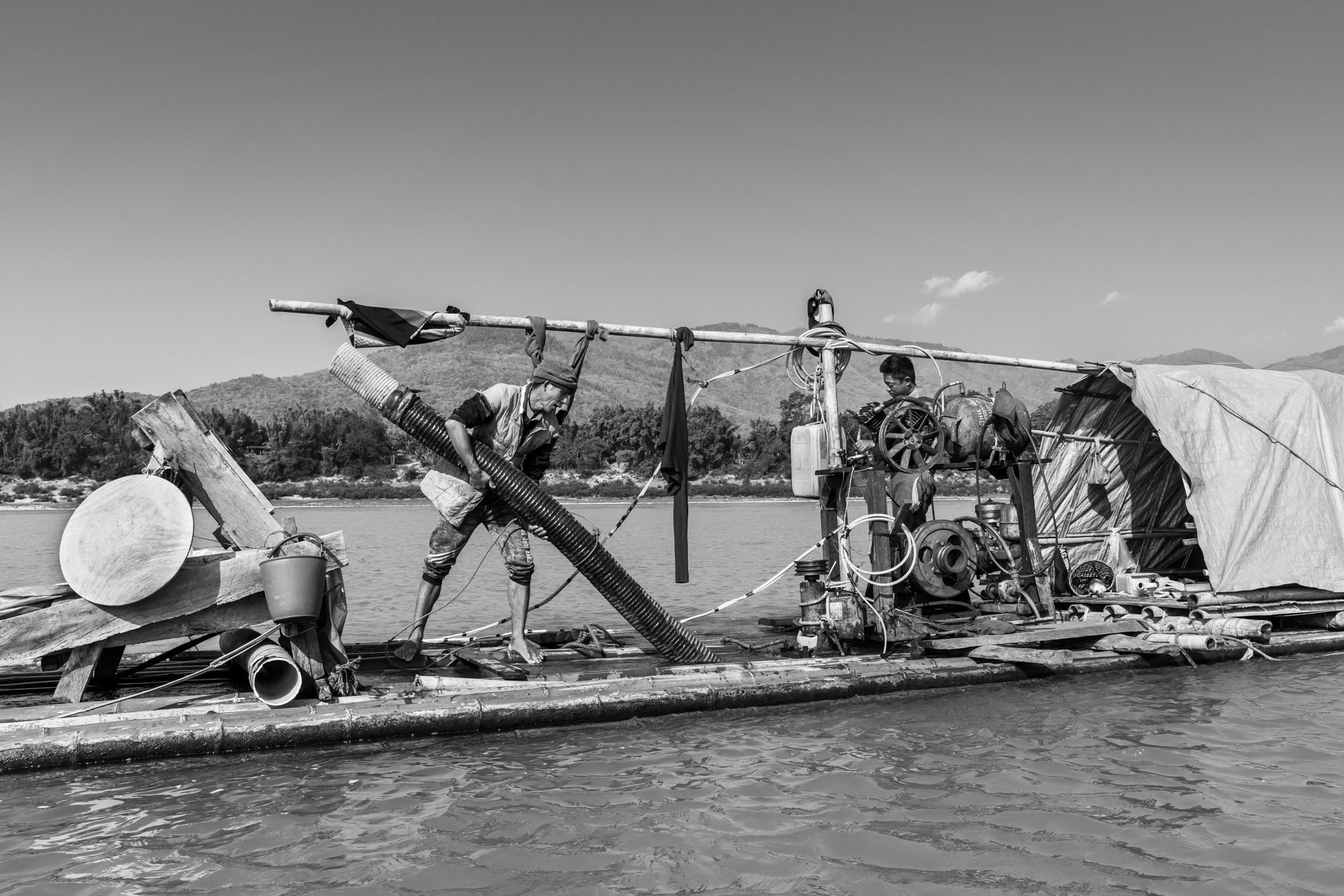 Raft used by local small scale gold divers. The season lasts from December to the end of March. One boat makes in average 60 to 80 USD per day and consists of 2 divers who dive 3-4 hours each, one in the morning and the other in the afternoon while the other stays on the raft. They dive at a depth of 10 to 15m with compressed air. Their equipment is extremely rudimentary and accidents occur frequently. They dive every single day in extremely strong currents and very cold water not exceeding 10-12C. With a large diametre hose they suck soil and sediments from the river bed up to the boat. Mercury, which is very toxic, is being used to make the gold stand out and blink. All the operations are done on the boat. Only people from the nearby villages are allowed to operate small scale gold digging activities, most of them are from the Lazi Kachin minority. Irrawaddy river north of Myitkyina, Kachin State, Myanmar, February 2020