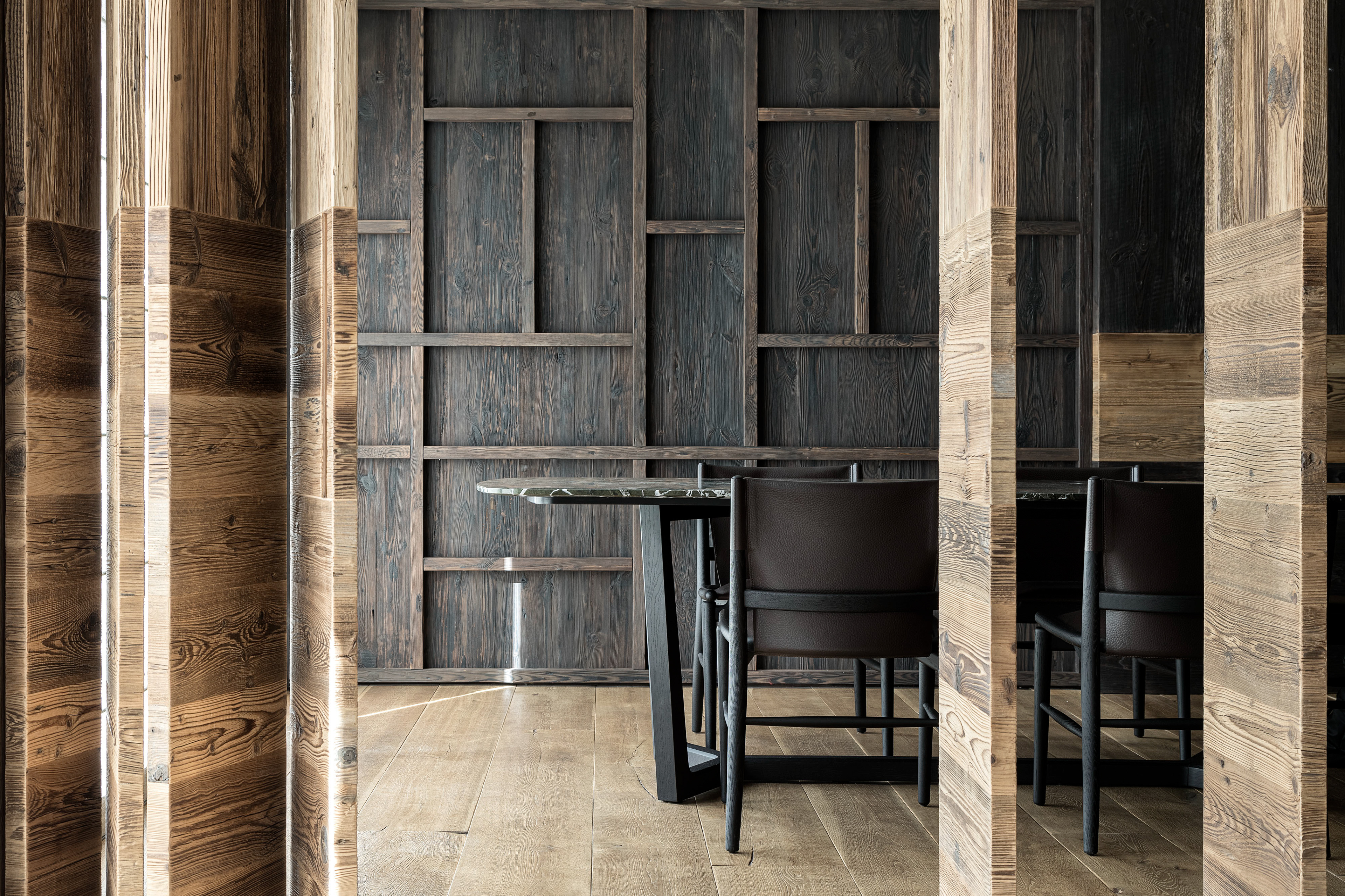 Elegant dining area with a backdrop of a wooden wall, highlighting refined design and warm materials in a luxury space.