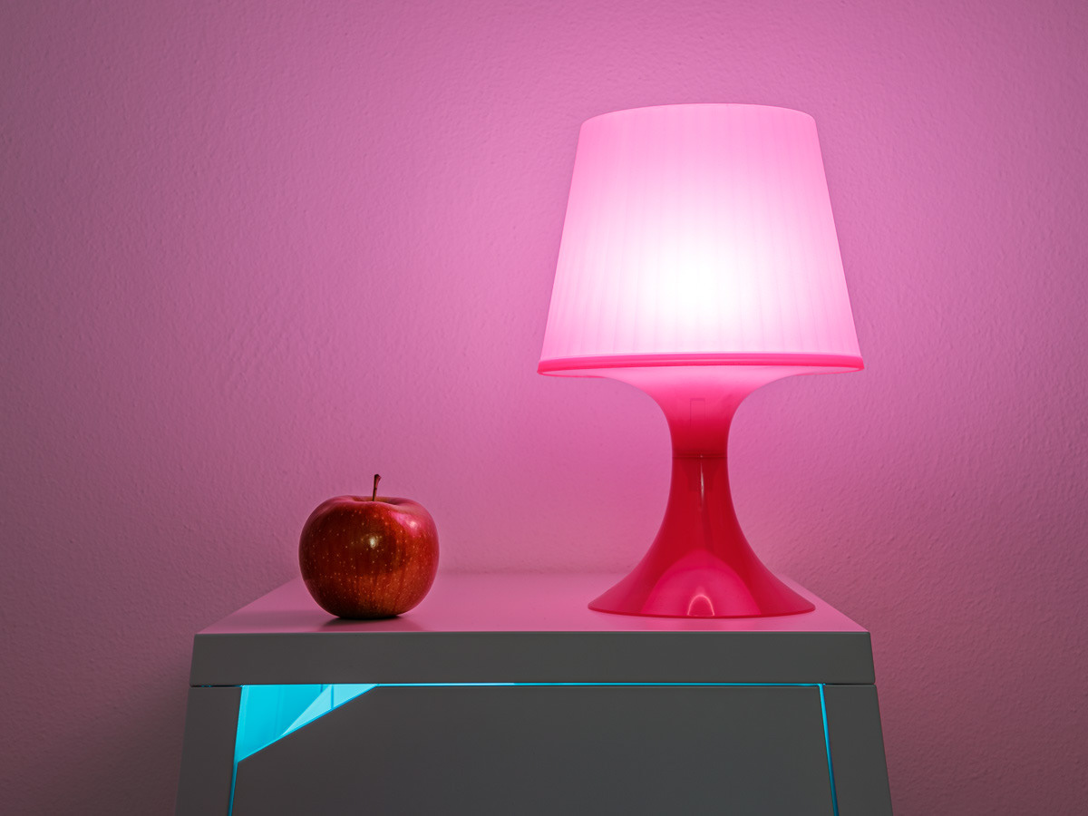 Lamp and red apple on a bedside table in violet light (still life, interior photography)