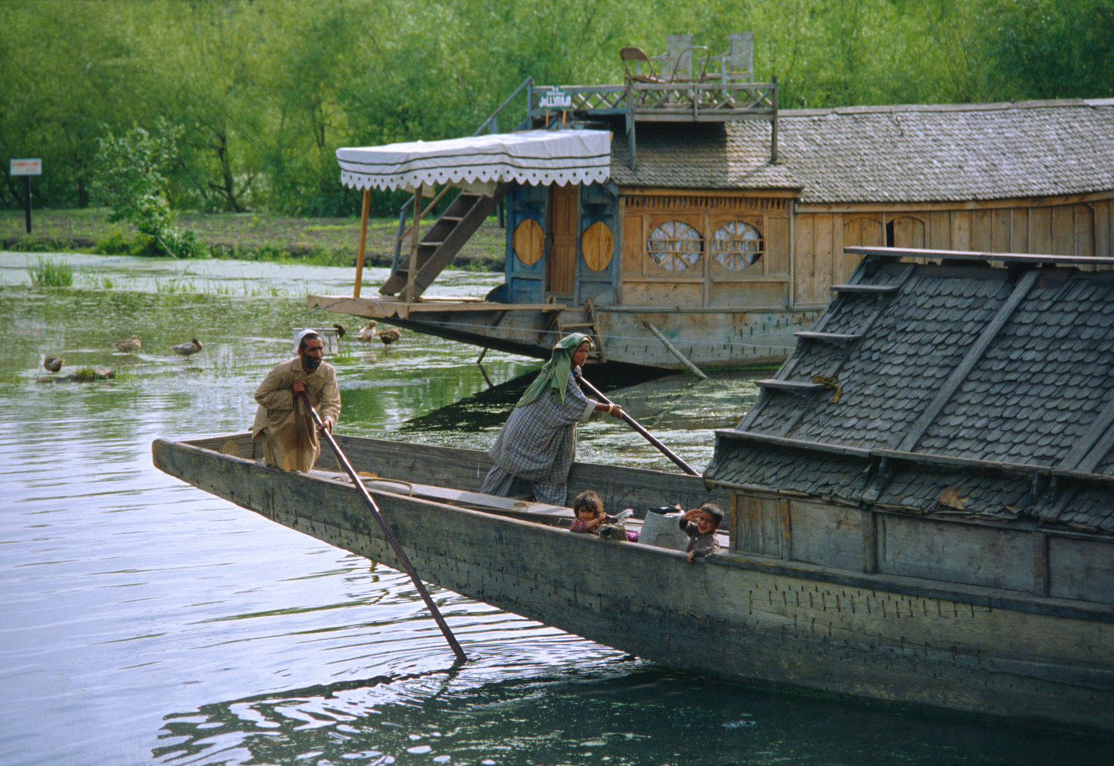 Family moving their houseboat on Dal Lake, Srinagar. Kashmir