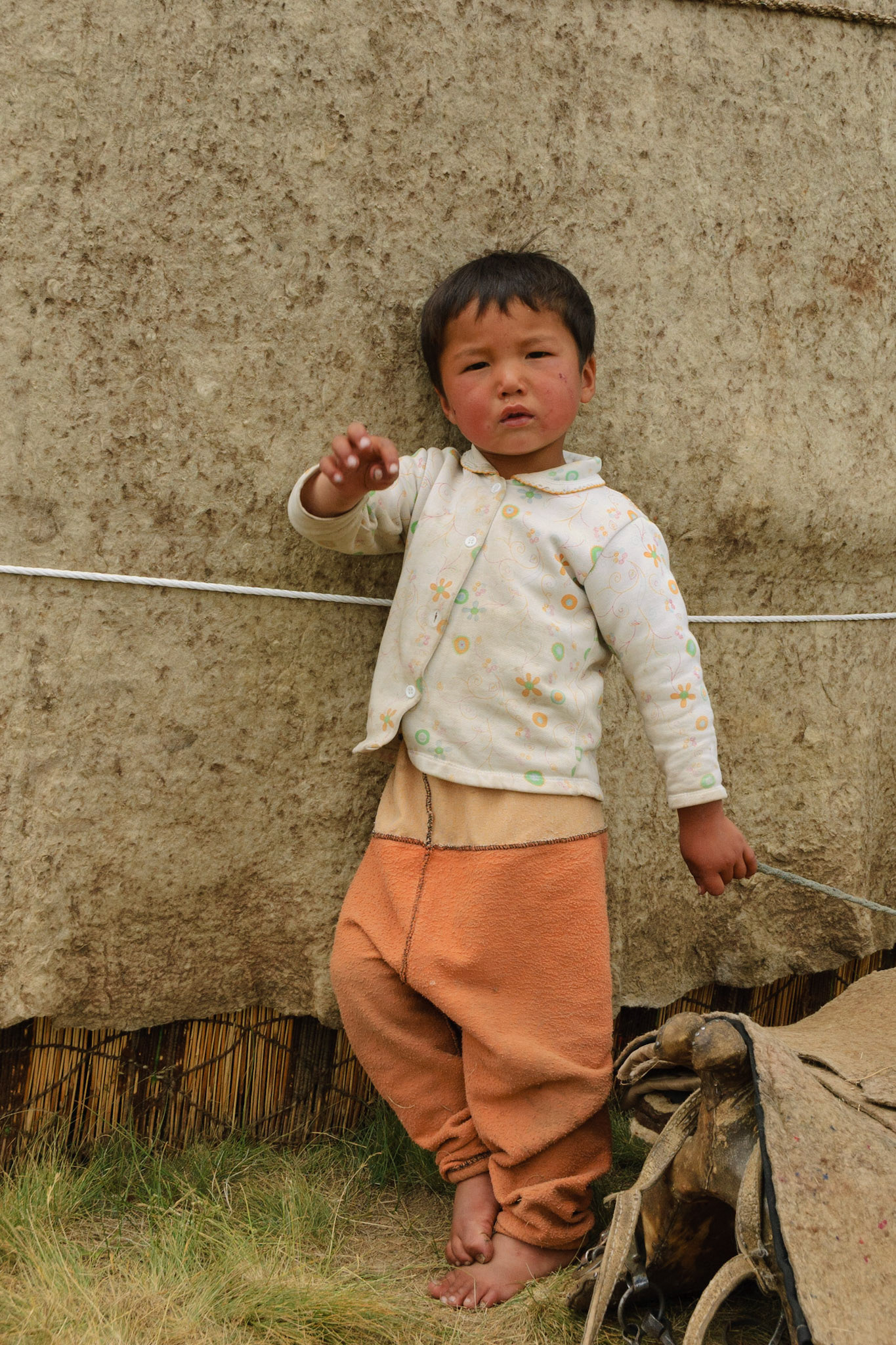 young boy playing with saddle, near lake Son Kul