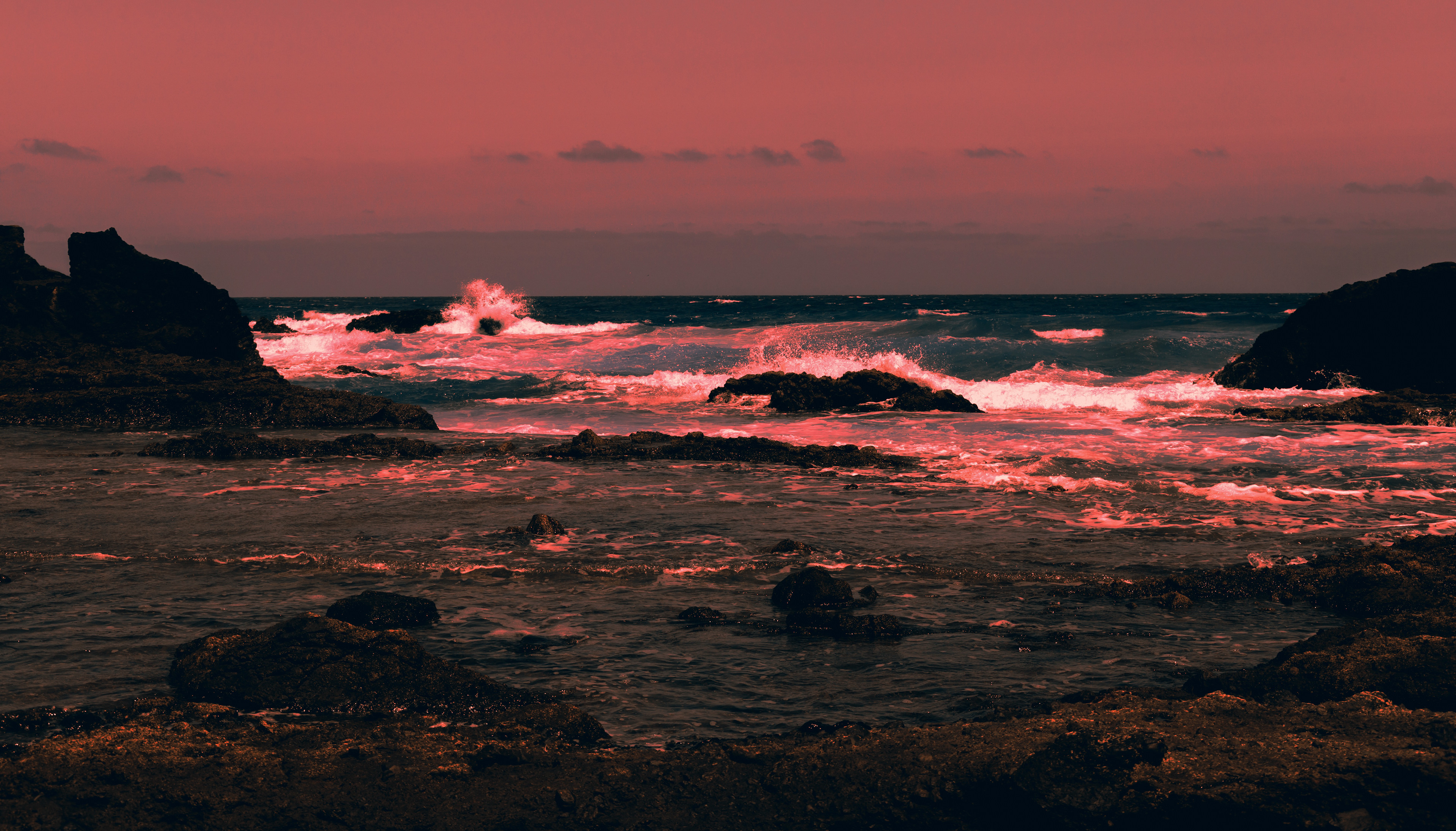 Vivid coral sunset over dark lava rocks on Fuerteventura’s coast—contrast of warmth and shadows.