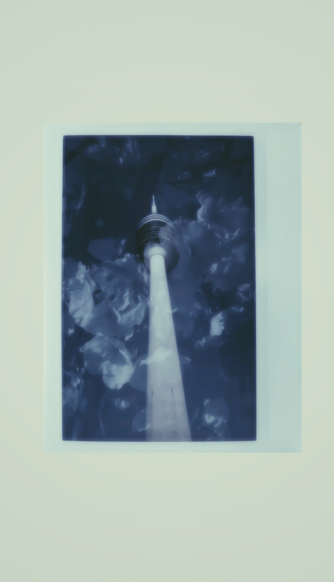 Moody analogue-style Polaroid of a broadcast tower set against cloud textures—captured with hybrid film camera and soft cyan tones.