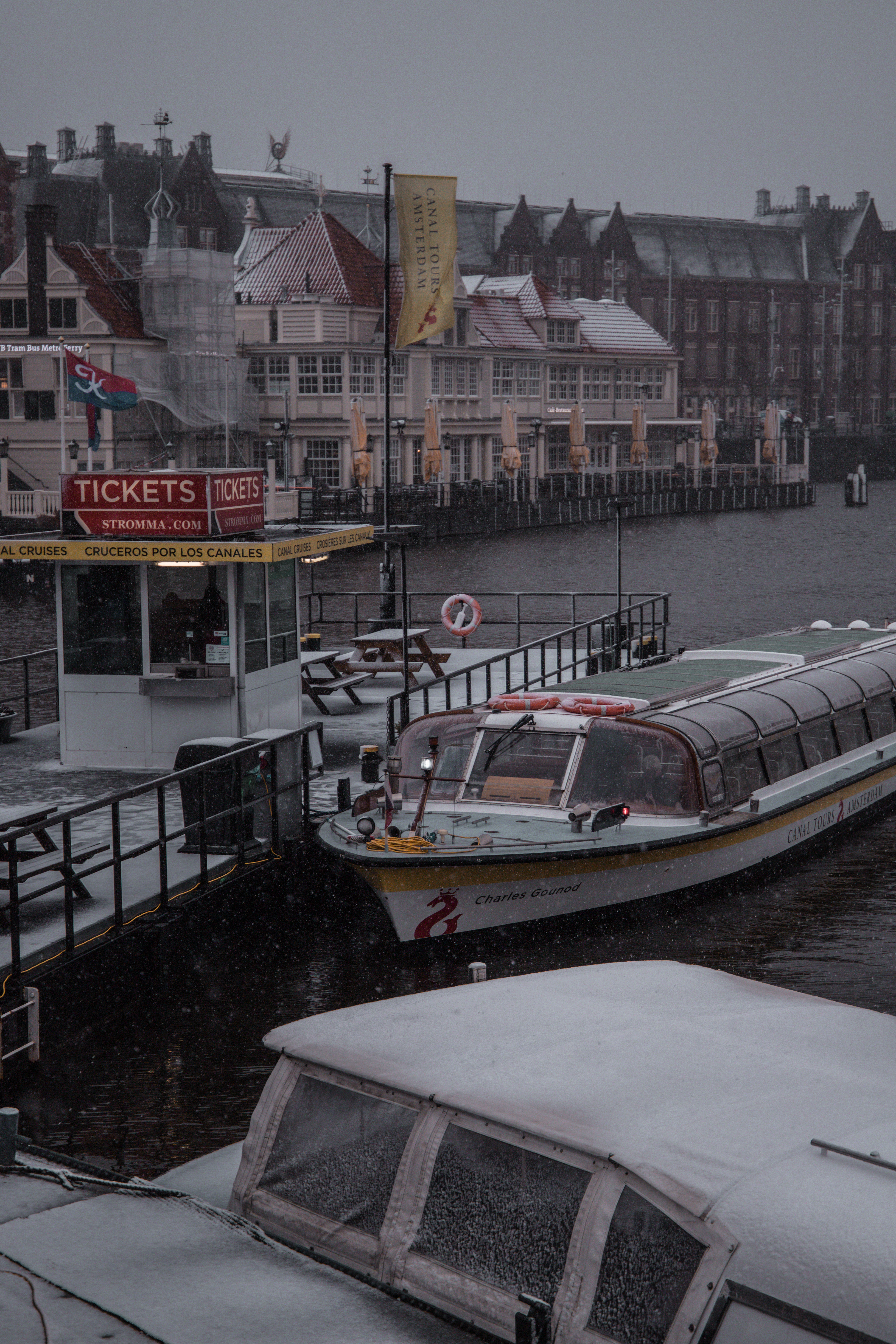Frozen boats and pier in central Amsterdam during unexpected snow—moody weather photography with city details.