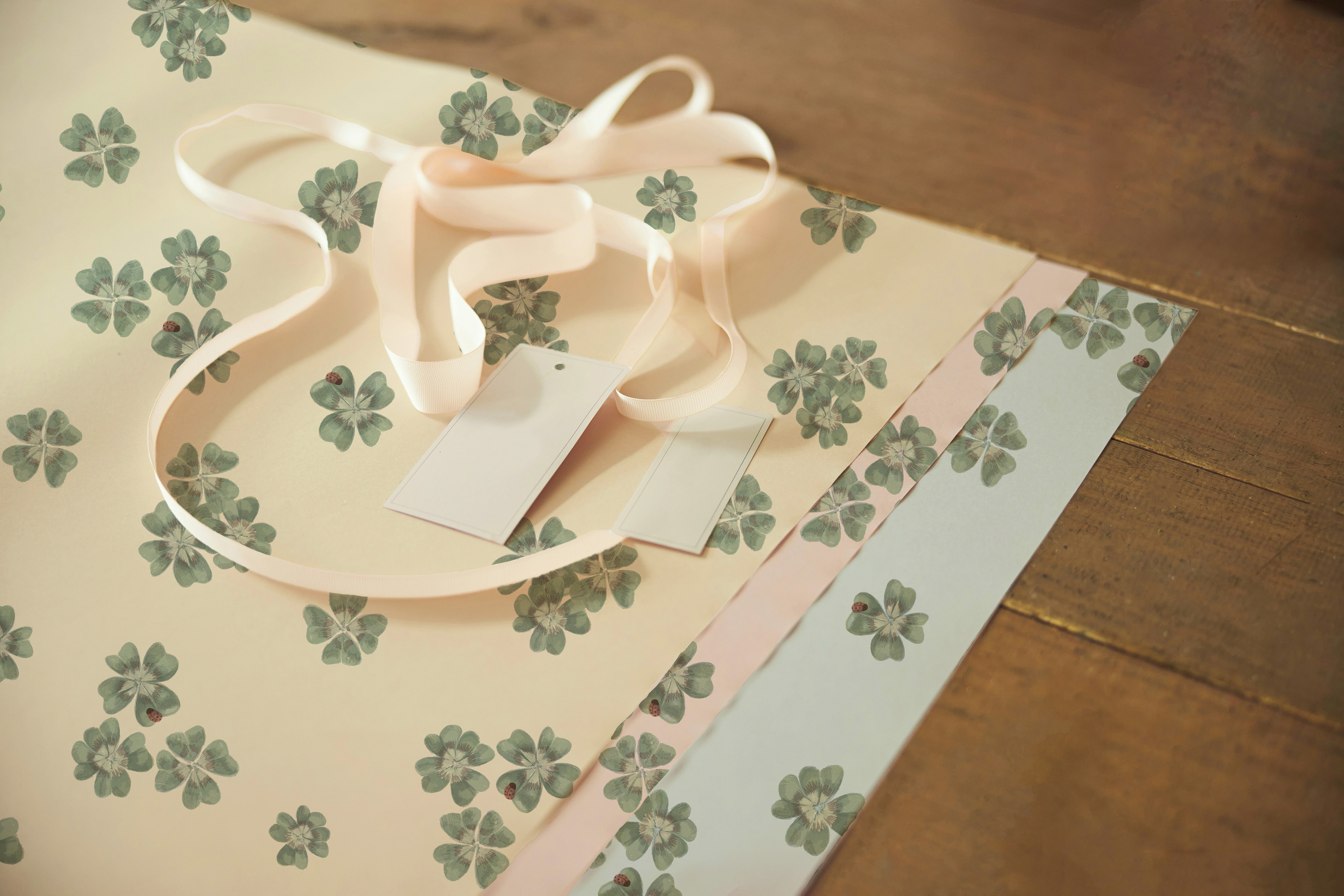 Flat lay of a gift bag or tote in Clover Scatter cream colourway with a white ribbon bow, on a warm wooden surface