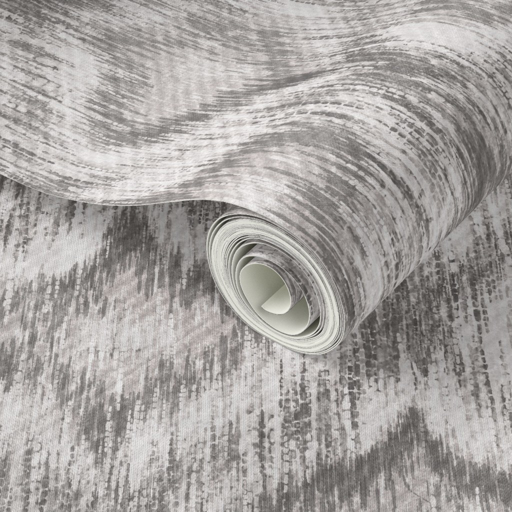 Rolled wallpaper sample of hand-painted ikat ogee pattern in soft grey with diffused organic edges, showing the woven texture of the grasscloth finish