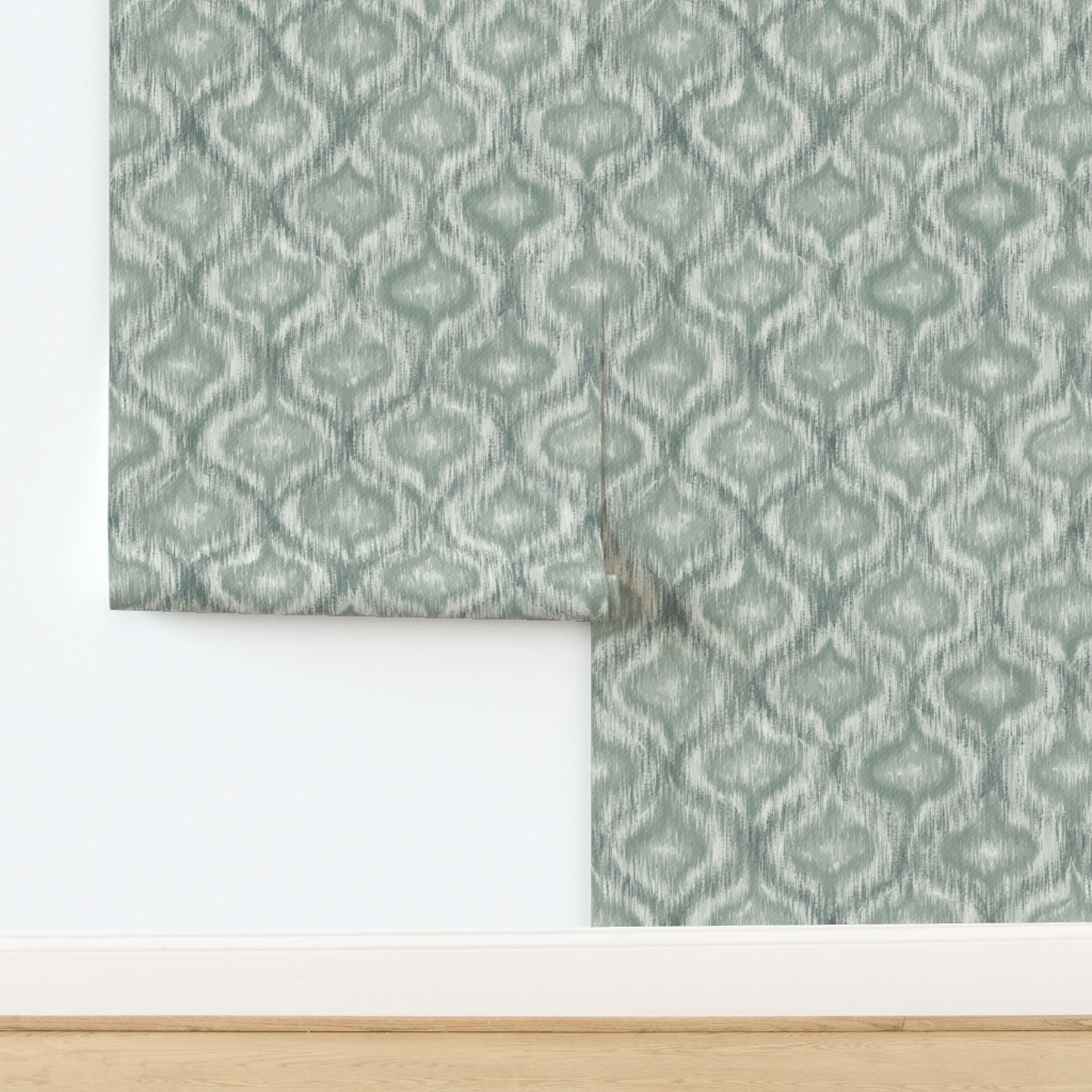 Dusty teal ikat ogee wallpaper panel propped against a white wall, showing the cool sage green colourway at room scale for a coastal or japandi bedroom