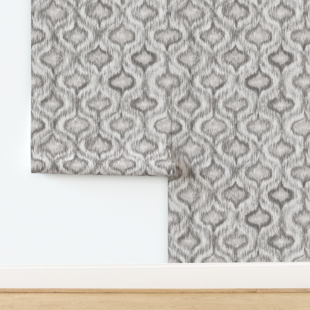 Wallpaper panel of grey ikat ogee pattern leaning against a white wall corner, showing scale and repeat for a hallway or bedroom feature wall