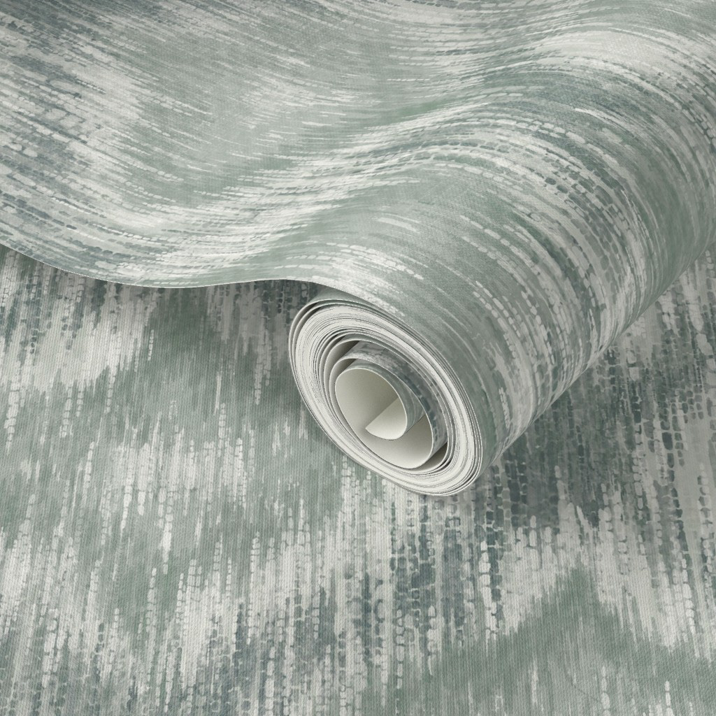 Rolled wallpaper sample of hand-painted ikat ogee in dusty teal and soft grey-green, showing the calm cool colourway and grasscloth texture finish