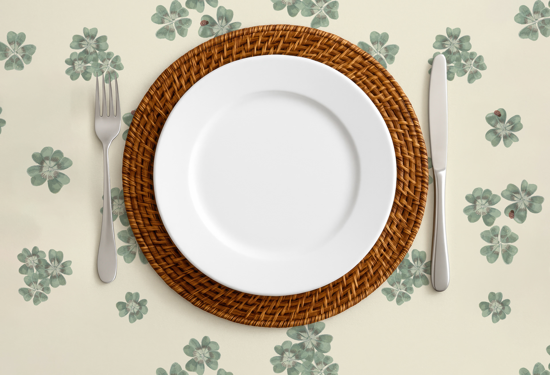 Table setting with Clover Scatter cream colourway placemat, a wicker charger plate and white dinner plate, fork and knife