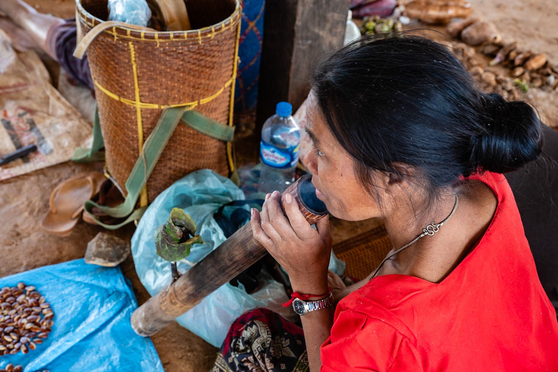 L'ethnie Katu vit dans des villages difficile d'accès, toujours clôturés avec une enceinte, faite avec des troncs d’arbres. Le village comporte dix à soixante maisons, construites sur des pilotis élevés à un mètre du sol. Là, je suis sur le plateau des Bolovens au sud du Laos. Cette femme Katu a travaillé toute la matinée au champ et vient sur la place centrale pour vendre le fruit de sa récolte. Traditionnellement, les femmes fument le tabac à toute heure de la journée à l'aide de leur pipe à eau, le khork’.