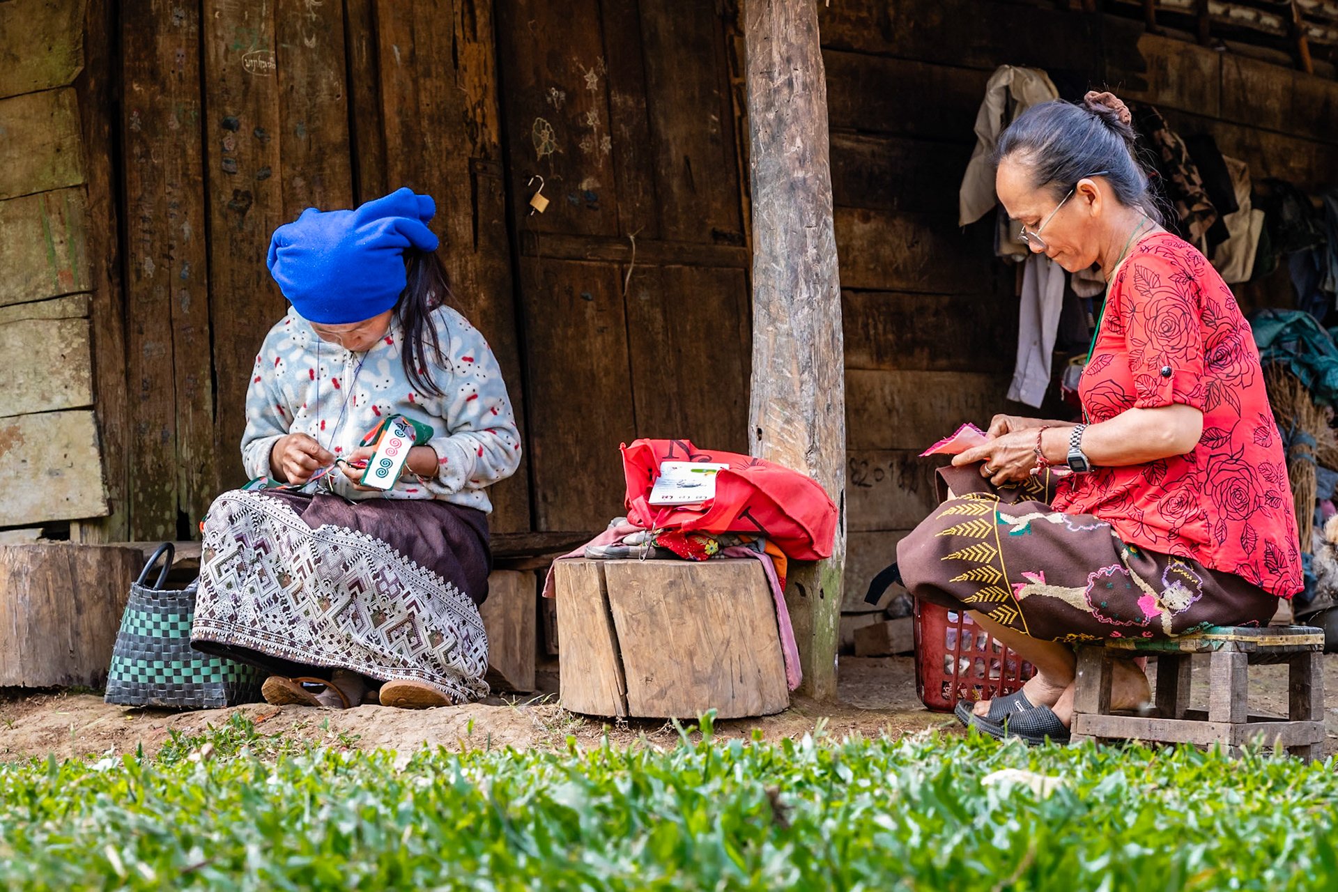 Sur leur pas de porte, ces deux femmes de l'ethnie Kamu font de la broderie pour décorer les vêtements ou proposer des parures d’ornement. Elles sont bien apprêtées, mais leurs habits ne sont pas totalement traditionnels. Il y a beaucoup de petits travaux artisanaux faits à la main dans ces villages de montagne, aux alentours de Luang Prabang.