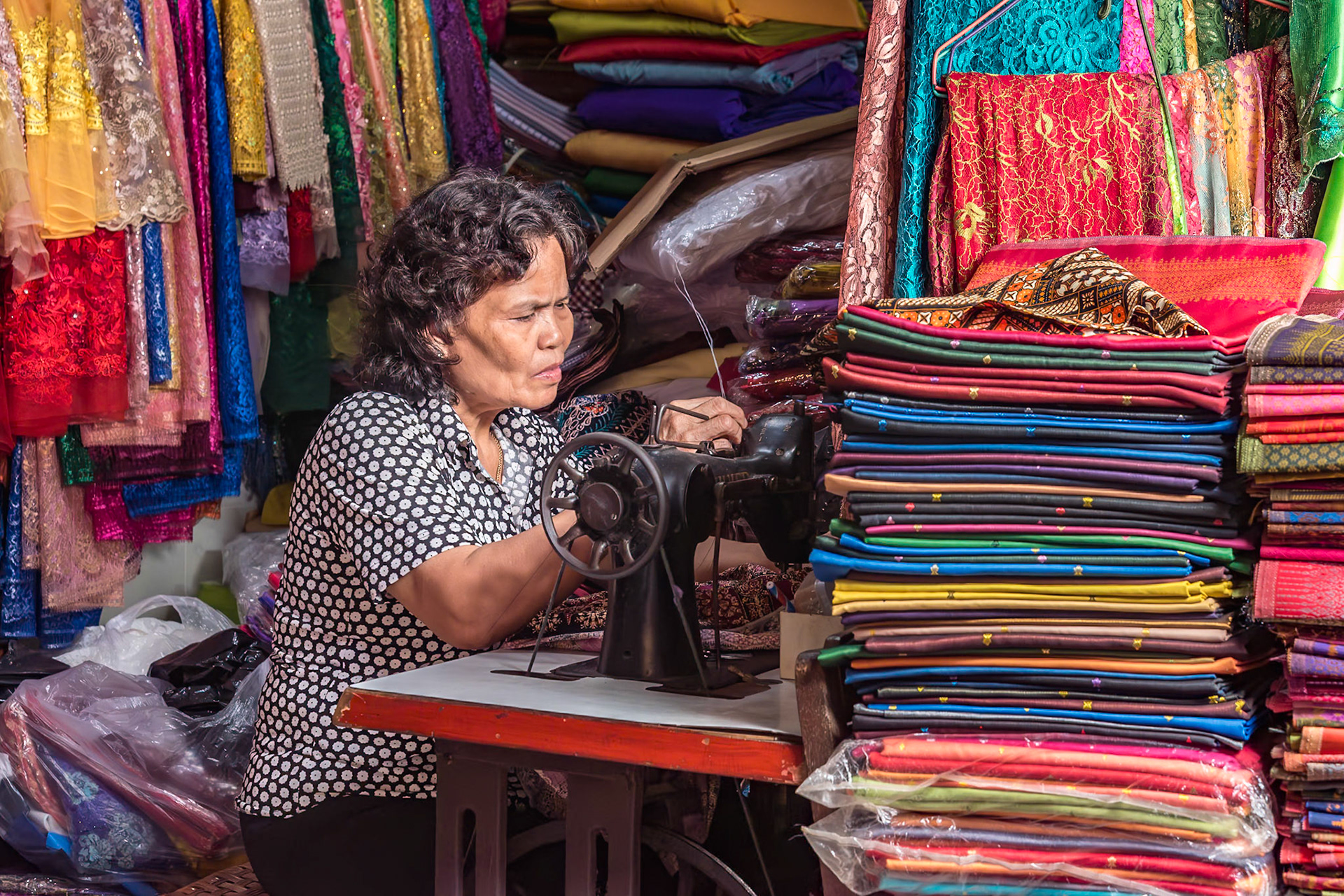 Je suis dans un dédale de petits couloirs du marché de Kampot, dans le Sud Ouest du Cambodge, et je rencontre beaucoup de personnes qui font des petits métiers aujourd'hui disparus en Europe. J'aurai pu vous proposer un horloger, un fabricant de bijoux, un réparateur de matériel hifi, ..... mais cette couturière dans son environnement multicolore a attiré mon objectif comme un aimant.