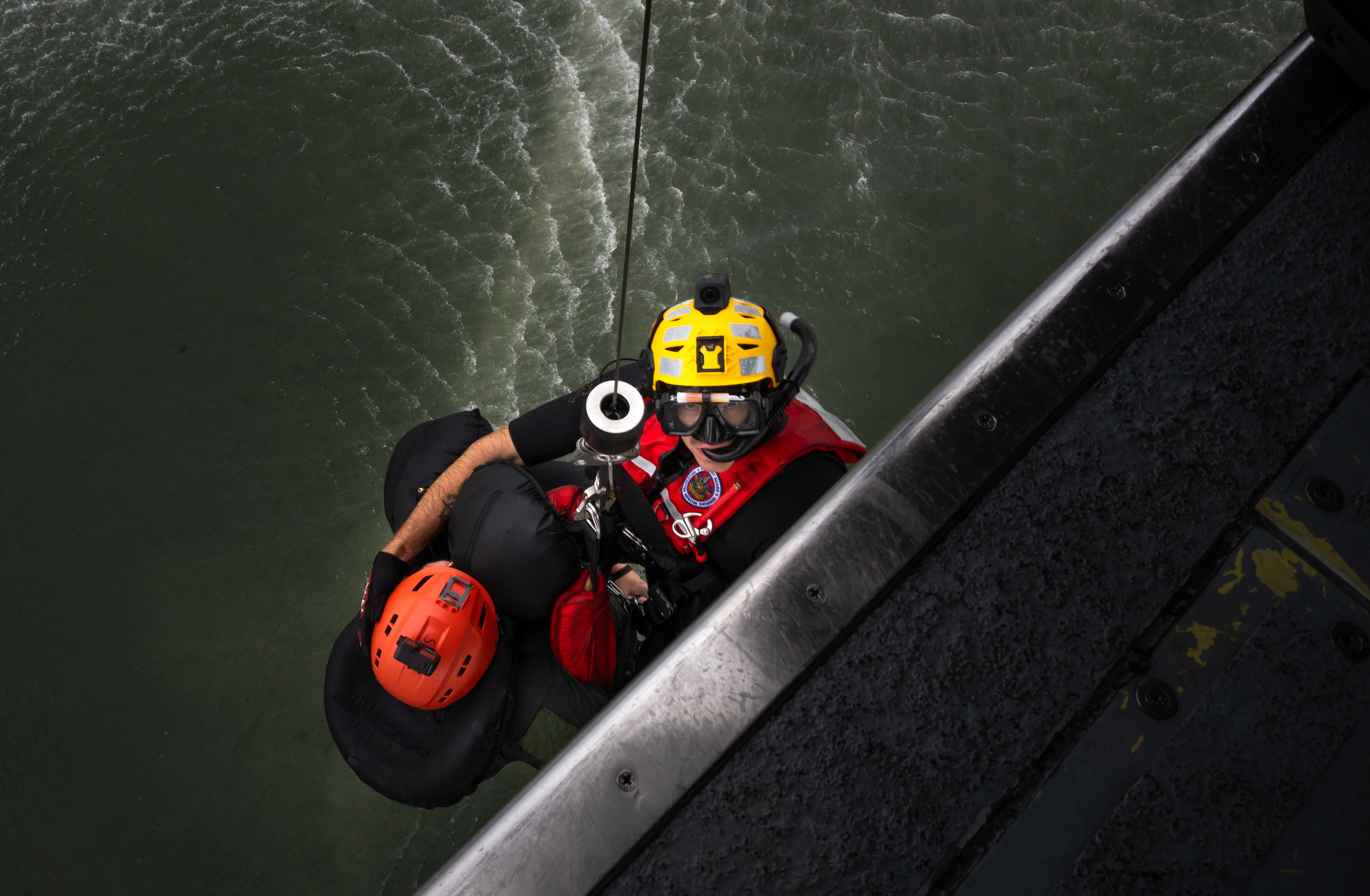 A U.S. Coast Guard rescue swimmer assigned to Air Station Elizabeth City carries U.S. Air Force Capt. Matthew Fuster, F-15E Strike Eagle weapons systems officer assigned to the 4th Fighter Wing, aboard an MH-60T Jayhawk helicopter, during a search-and-rescue exercise over Cape Hatteras, North Carolina, Aug. 28, 2025. The exercise evaluated recovery procedures for pilots who are injured or stranded.