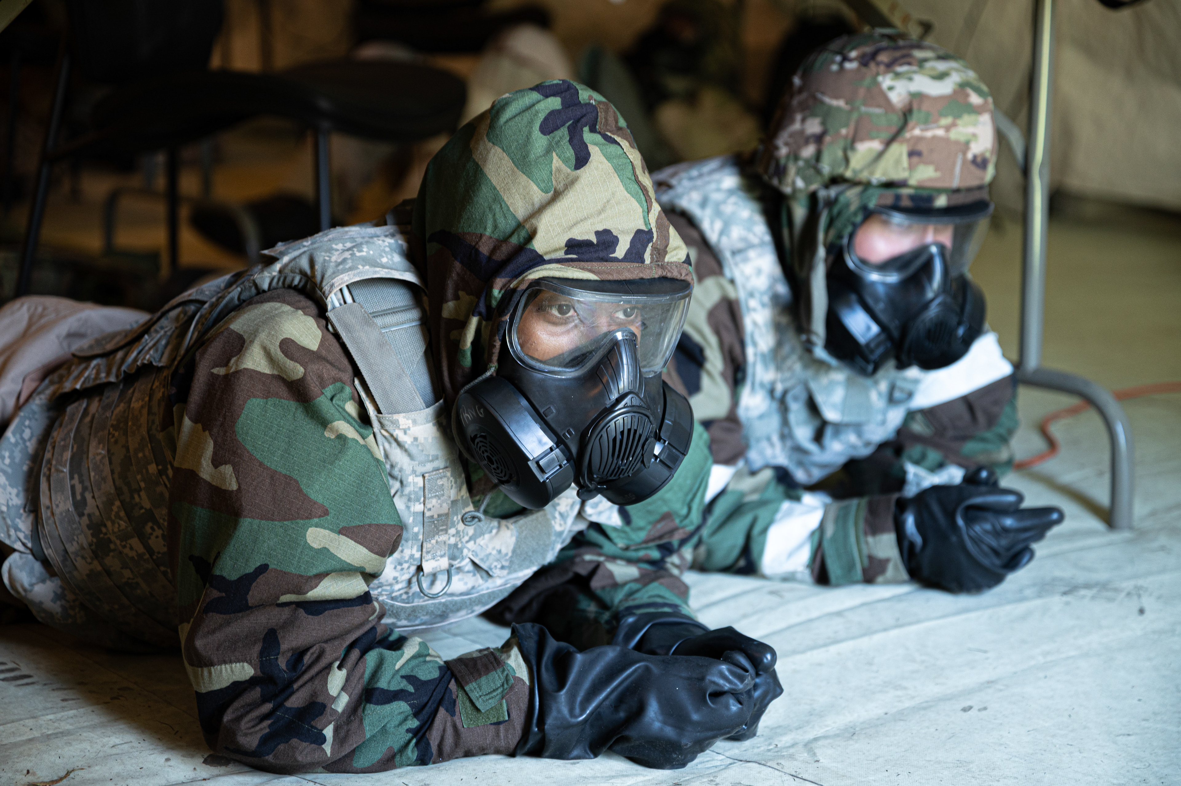 U.S. Air Force Airman 1st Class Ahmed Abdirahman, 4th Comptroller Squadron finance operations technician, ducks under a table while wearing full Mission Oriented Protective Posture (MOPP) gear during a simulated attack drill at Seymour Johnson Air Force Base, North Carolina, May 20, 2025. The exercise tested the Airmen’s ability to maintain mission focus and seek cover during chemical, biological, radiological, and nuclear (CBRN) scenarios.
