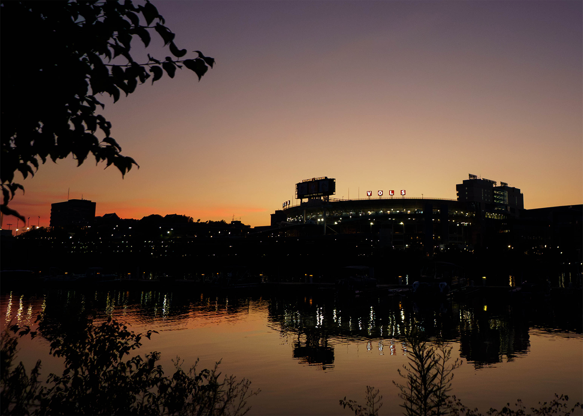 Neyland Stadium is silhouetted by an orange sunset as seen from across the Tennessee River.  (Photo by Miles Lineberger / Tennessee Football)