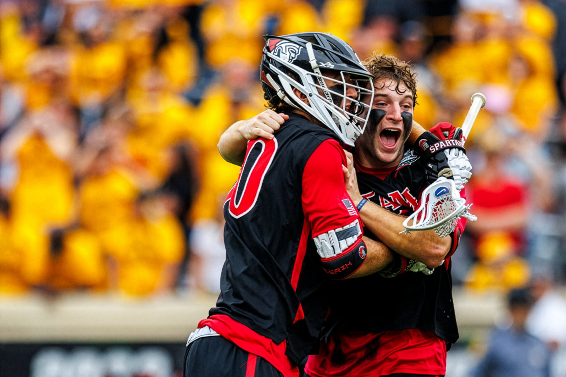 Tampa Spartans lacrosse players embrace after Tampa's 12-11 overtime win in the 2026 NCAA Division II Men's Lacrosse Championship at Scott Stadium on May 24, 2026.  (Photo by Miles Lineberger / Adelphi University)