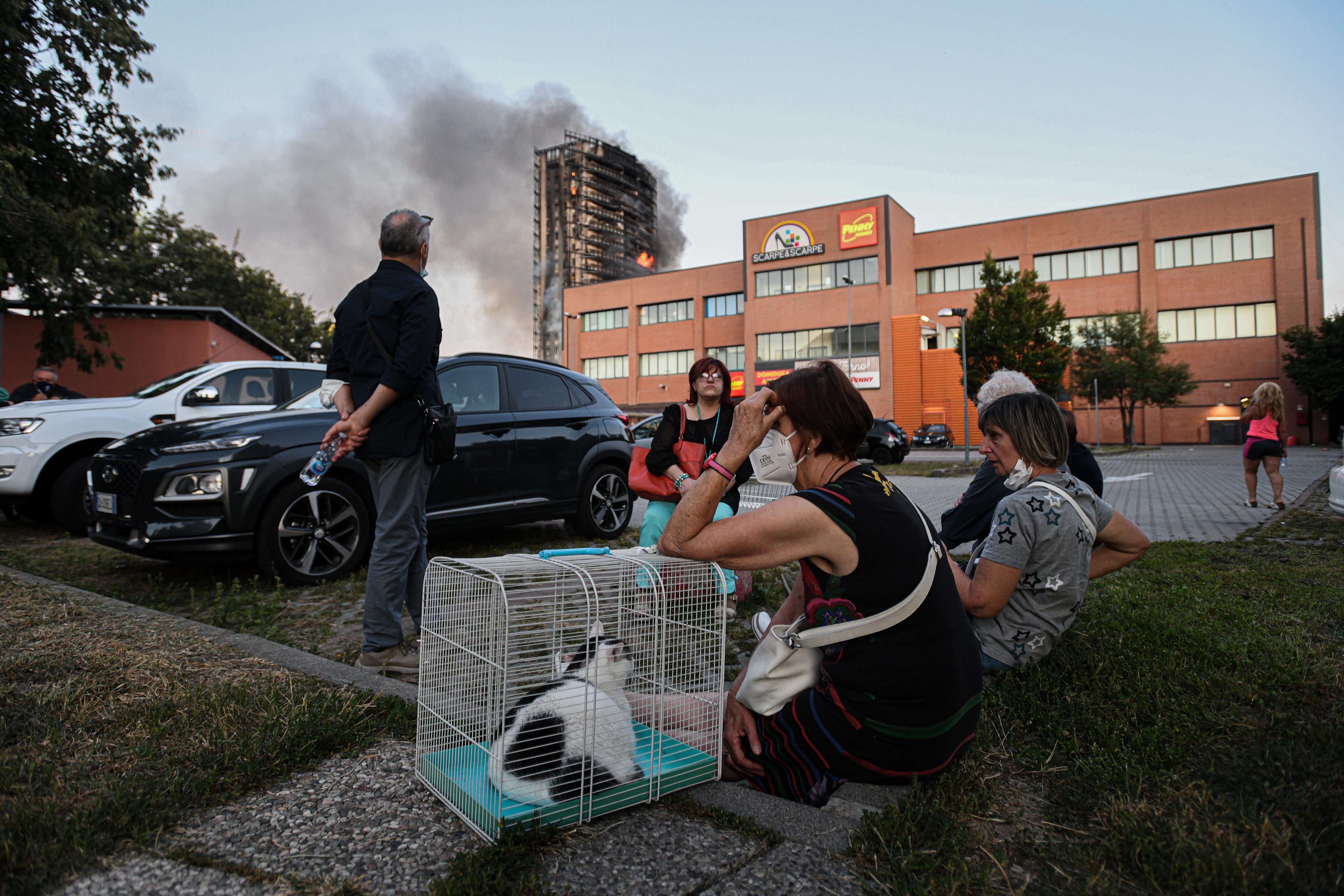 People sit on the grass in front of a 20 storey residential building being ravaged by a fire in Milan on August 29, 2021 . The building located in the southern outskirts of the Lombard capital caught fire in the upper floors around 5.30 pm. "The flames then spread to the lower levels," causing thick smoke, the firefighters said on their Twitter account. Piero CRUCIATTI / AFP fotografo milano photographer milan