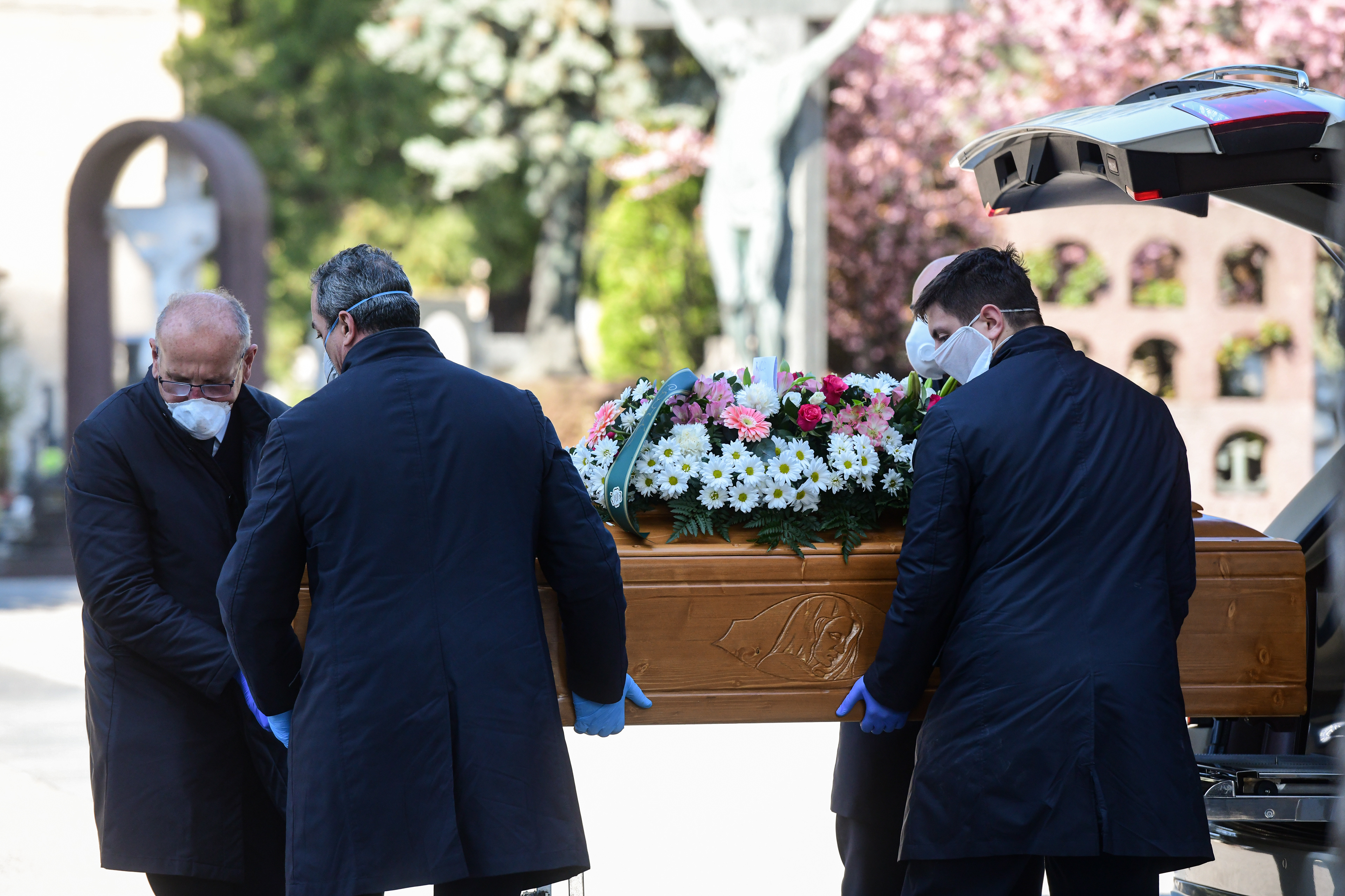 Bergamo, Italy - 16 March 2020: Men wearing face masks unload a coffin from a hearse at the Monumental Cemetery