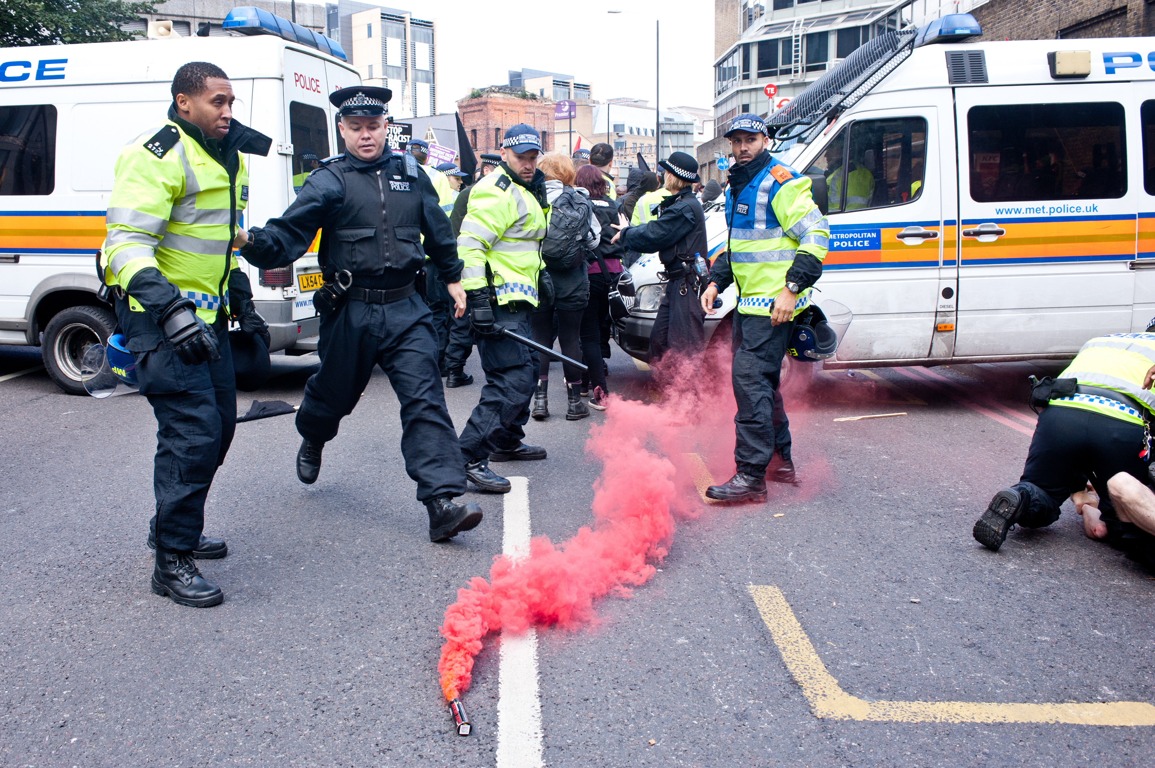 London, UK - 7 September 2013: a police officer runs towards a smoke pot as anti-EDL protester try to break the police line. 