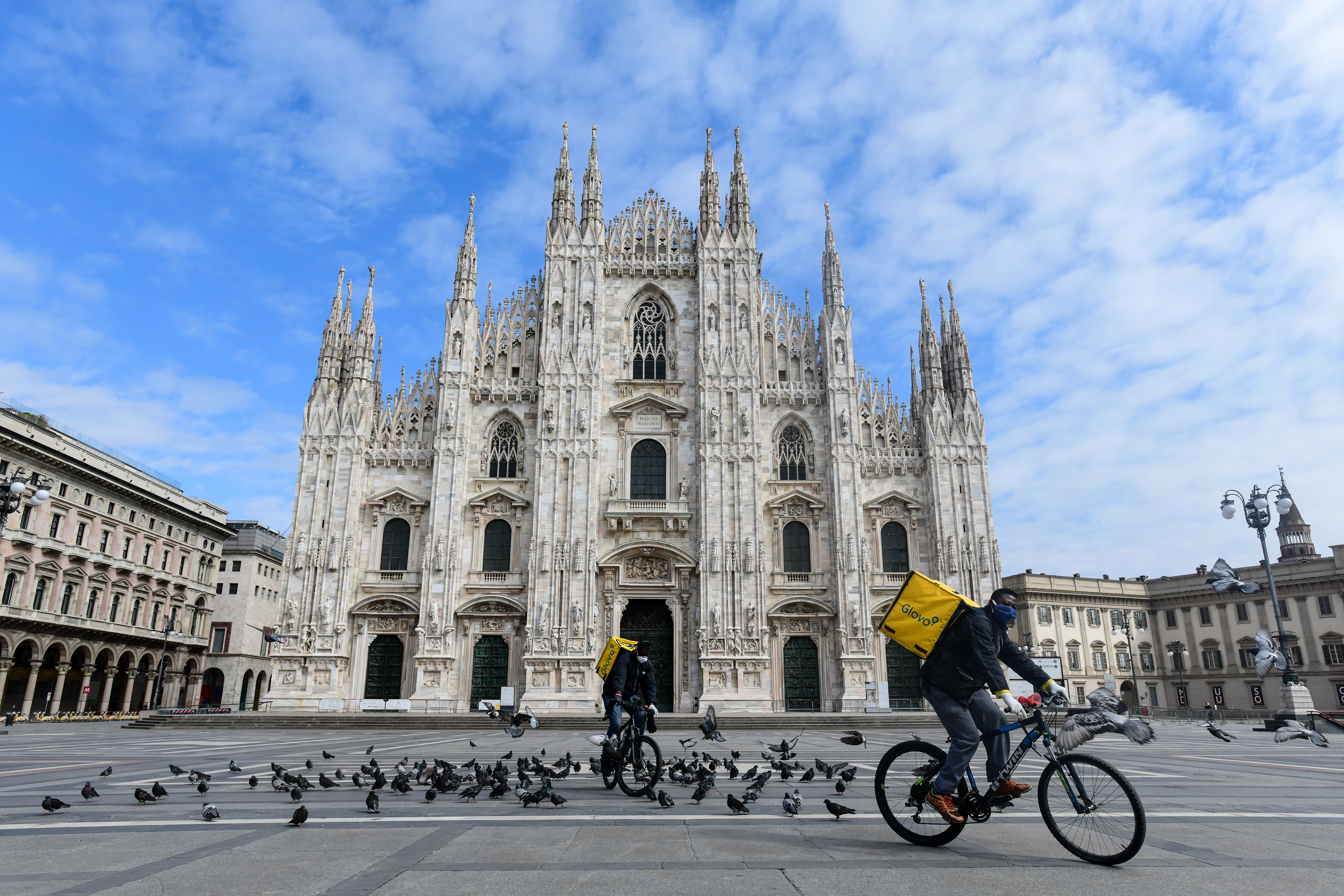 Two cyclists working for the food delivery service Glovo ride their bike in a deserted Piazza Duomo in Milan, Italy on March 31, 2020 