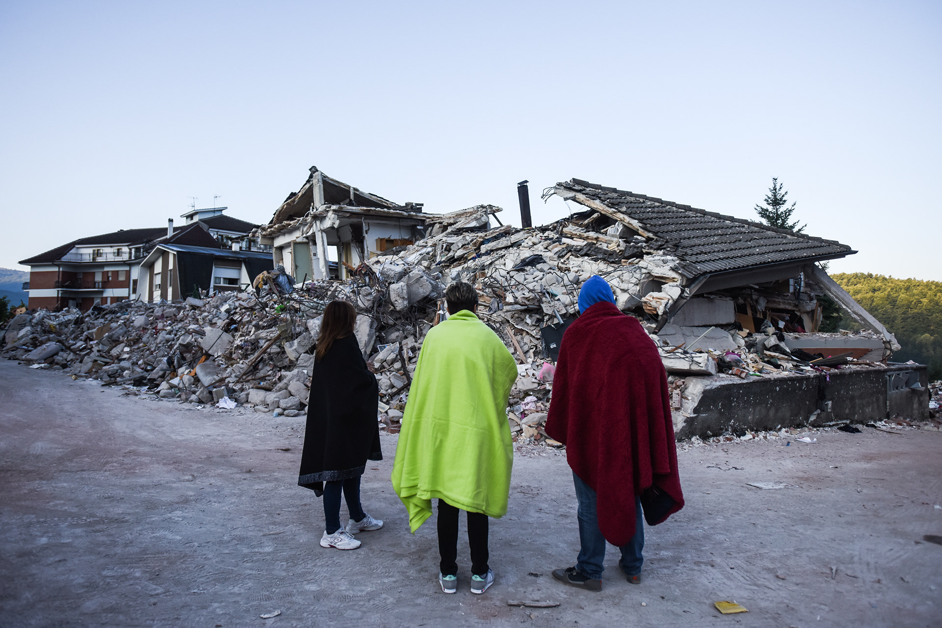 people stand in front of destroyed houses following a powerful earthquake in Central Italy