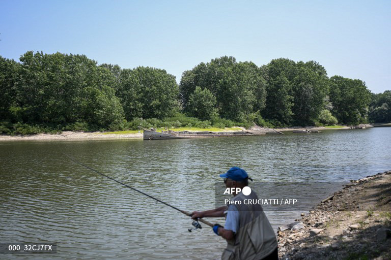 A man fishes at the site where a large 55-meter barge (Rear) that was sunk by WWII American bombing in 1944 while preventing retreat of the German army, re-emerged due to severe drought from the River Po in Gualtieri, Italy on June 15, 2022. According to the river observatory, the drought affecting Italy's longest river Po is the worst in the last 70 years. (Photo by Piero CRUCIATTI / AFP)