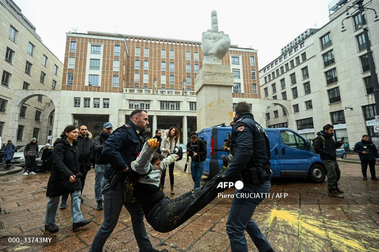 Police officers carry a Ultima Generazione (Last Generation) environmental activist after he threw washable paint to Maurizio Cattelan’s "L.O.V.E." artwork in front of the Palazzo Mezzanotte, seat of the Italian stock exchange, in Piazza Affari in Milan, on January 15, 2023, to raise awareness on climate change. (Photo by Piero CRUCIATTI / AFP) / RESTRICTED TO EDITORIAL USE - MANDATORY MENTION OF THE ARTIST UPON PUBLICATION - TO ILLUSTRATE THE EVENT AS SPECIFIED IN THE CAPTION