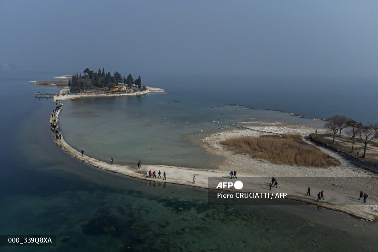 An aerial photo shows the small island of San Biagio, off Manerba del Garda, Lake Garda, on February 21, 2023, where the water level dropped to its lowest in 30 years during the winter months. A lack of snow on the surrounding mountain peaks, the absence of rain for the past six weeks, and mild temperatures - this explosive cocktail has caused the water level of Italy's largest lake to drop to its lowest in 30 years during the winter months. (Photo by Piero CRUCIATTI / AFP)