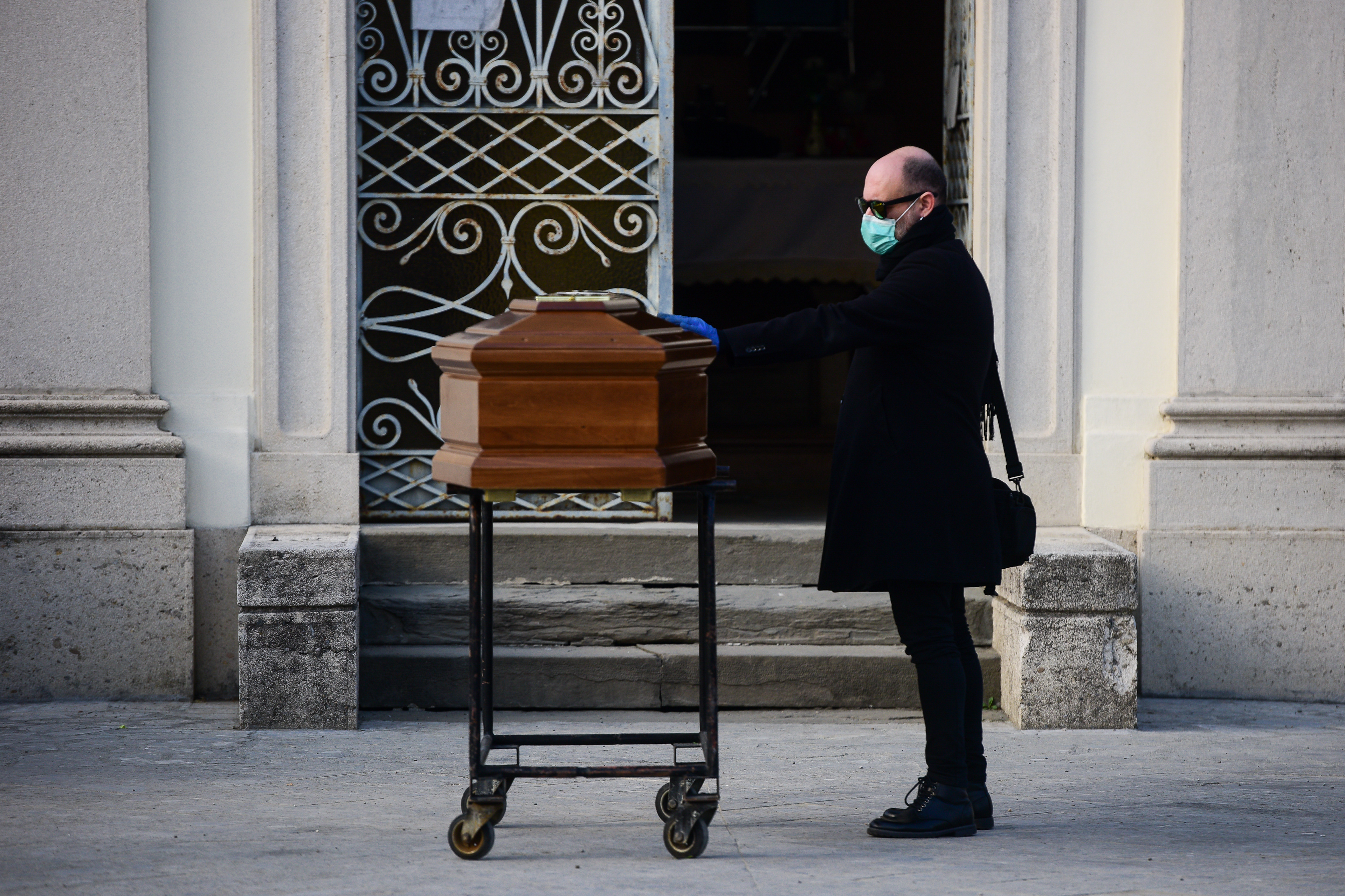 A man touches the coffin bringing the body of her mother during a closed-doors funeral service in the cemetery of Seriate, Italy on March 20, 2020