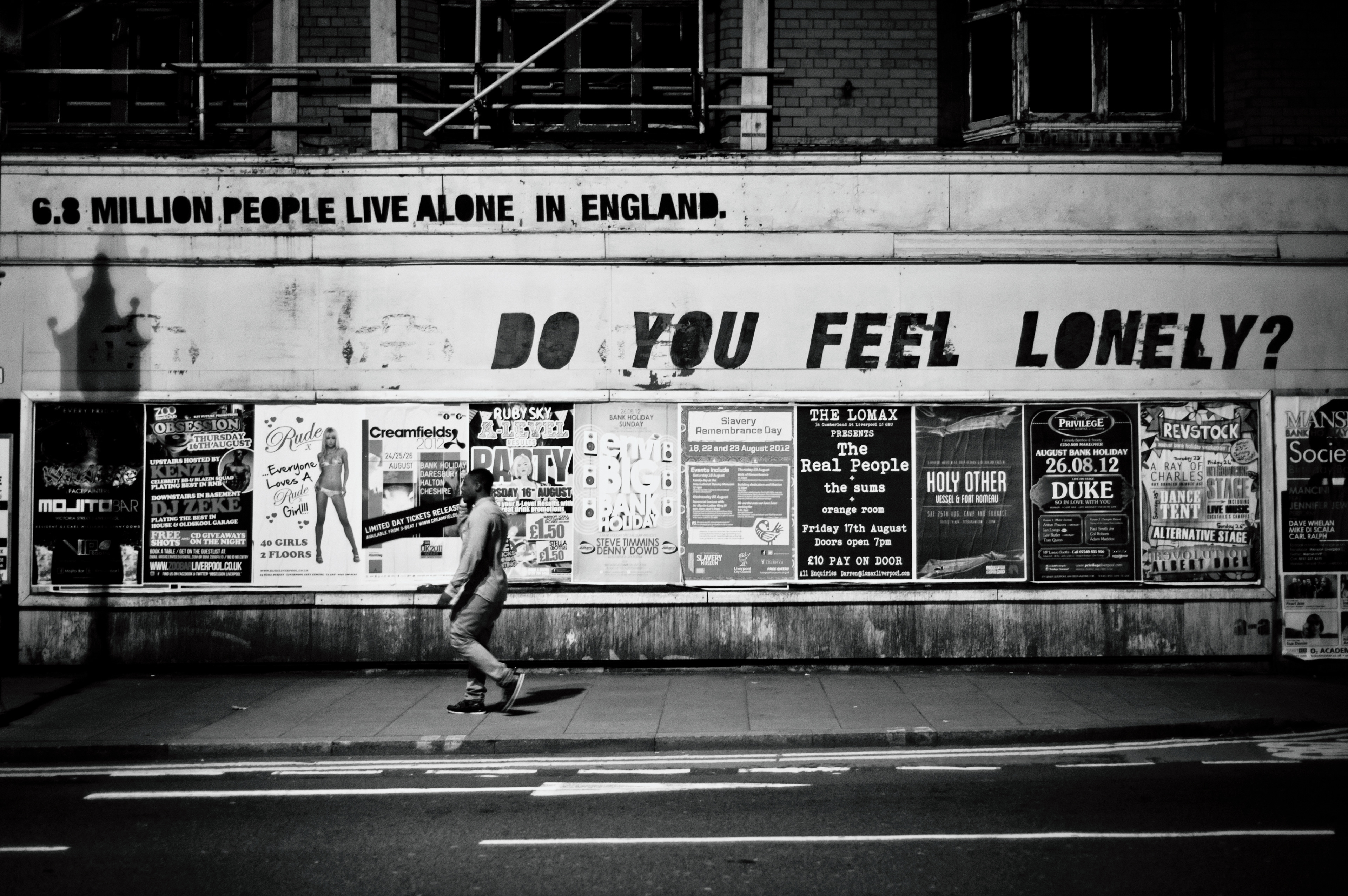 Liverpool, UK - 16 August 2012: A man walks by a graffiti at night reading '6.8 million people live alone, in England. do you feel lonely?'