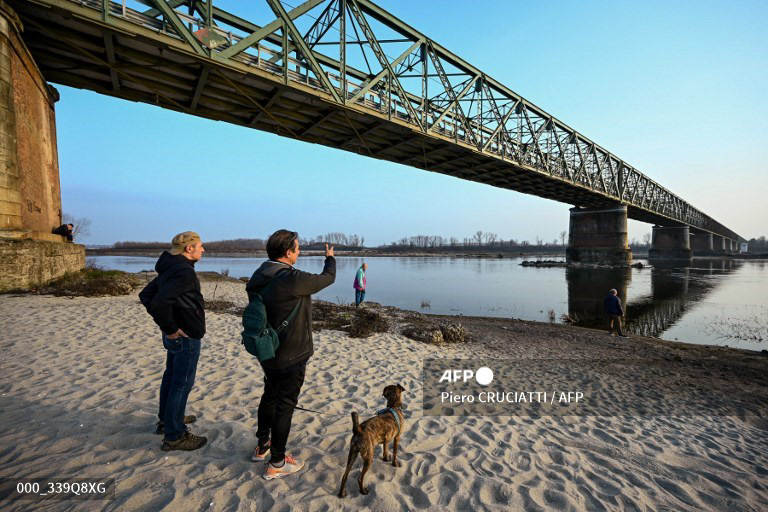 People take photos by the riverbed of the river Po on February 21, 2023 at Ponte della Becca, in Linarolo, near Pavia. A lack of snow on the surrounding mountain peaks, the absence of rain for the past six weeks, and mild temperatures - this explosive cocktail has caused the water level of Italy's largest lake to drop to its lowest in 30 years during the winter months. (Photo by Piero CRUCIATTI / AFP) 