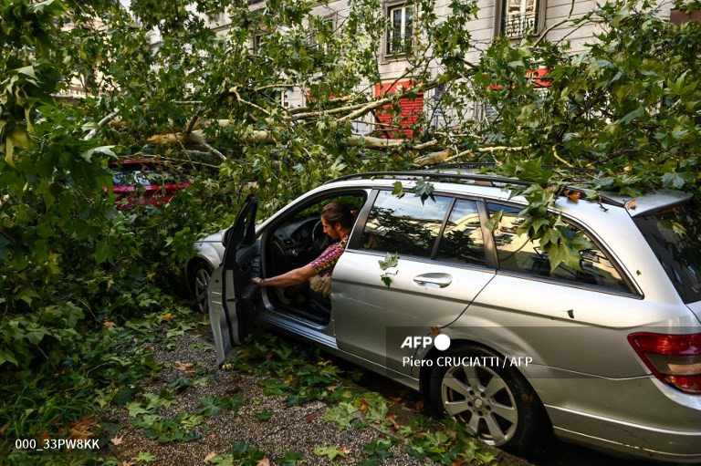 A resident attempts to remove his car stuck under fall tree branches in Milan on July 25, 2023 after an overnight rainstorm hit the city. (Photo by Piero CRUCIATTI / AFP)