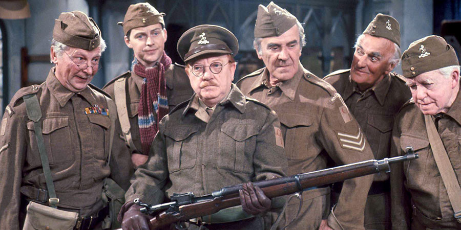 A still from the TV programme Dad's Army with the cast all showing all looking at a rifle