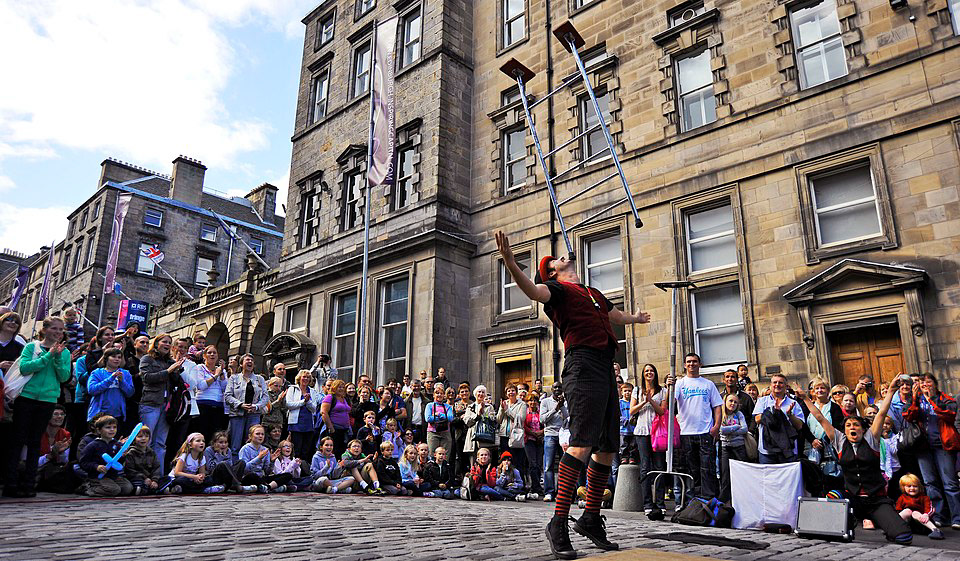 A street performer balancing a ladder on his chin surrounded by a crowd at the Edinburgh Fringe Festival