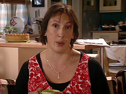The character Miranda from the TV show of the same name mid conversation to audience in her kitchen