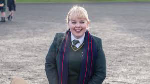 Clare Devlin at school, grinning widely from the show Derry Girls