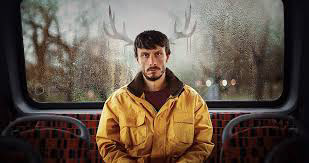 Image of Richard Gadd sat at the back of a bus with what appears to be reindeer antlers