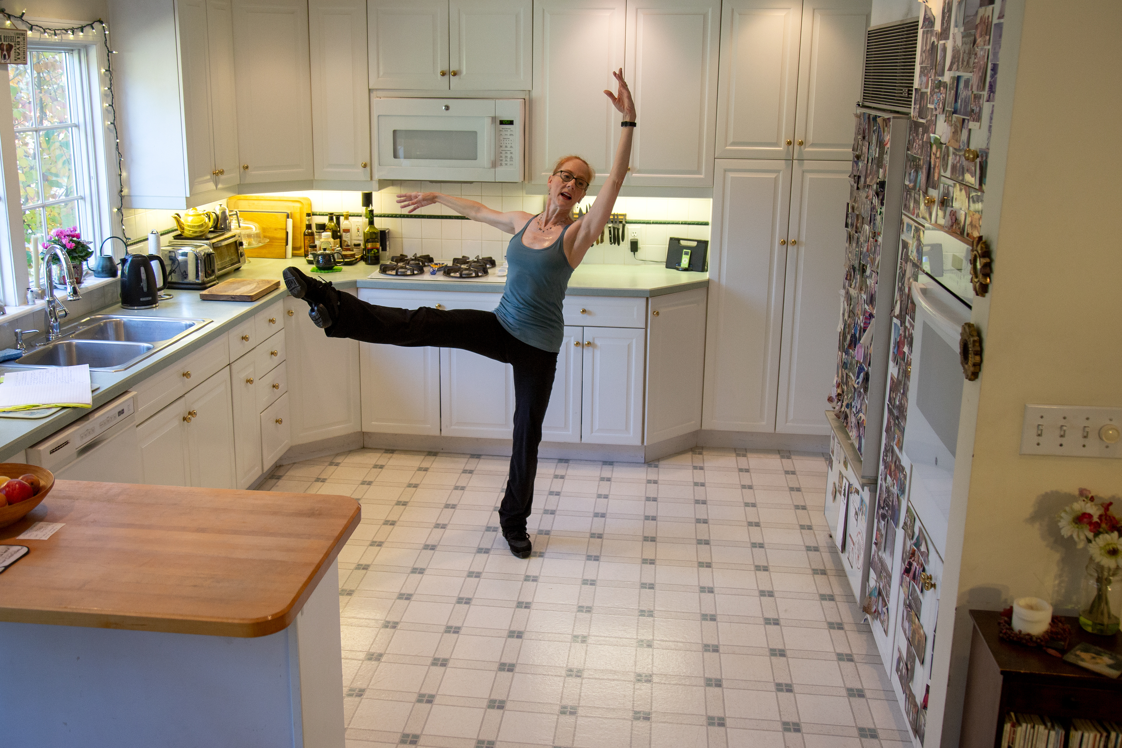 A ballet dancer kicks up a leg in a kitchen