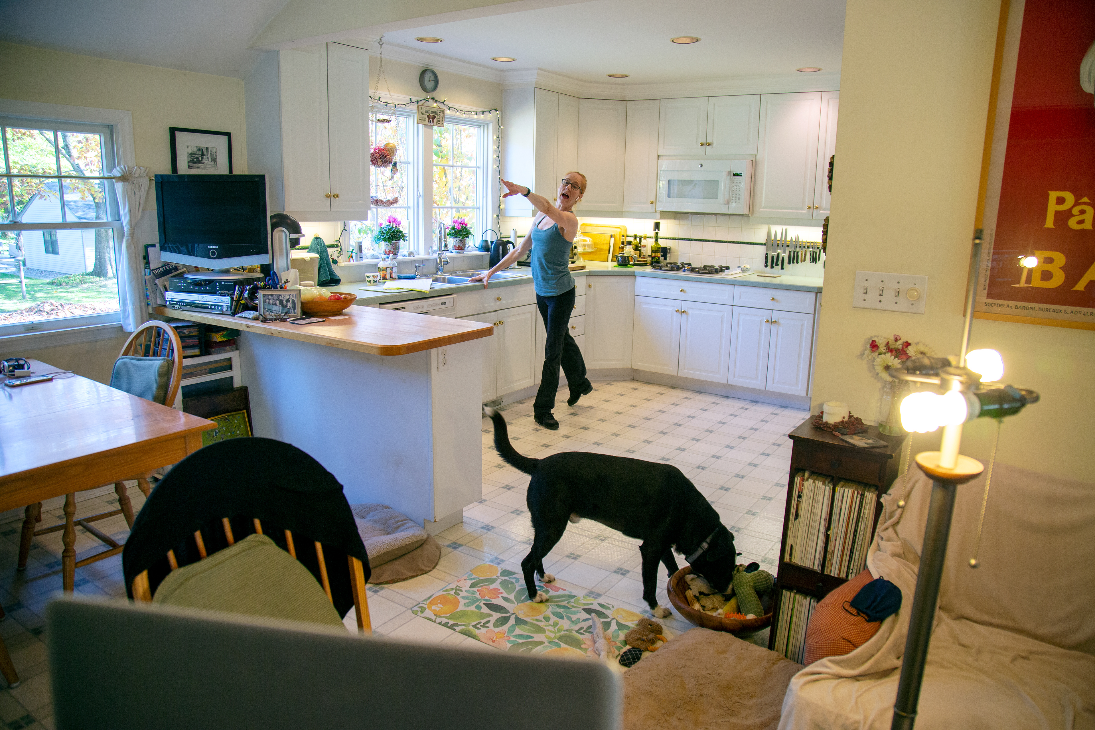 A dancer has her hand on a kitchen counter top as she stretches arm out and a leg back.
