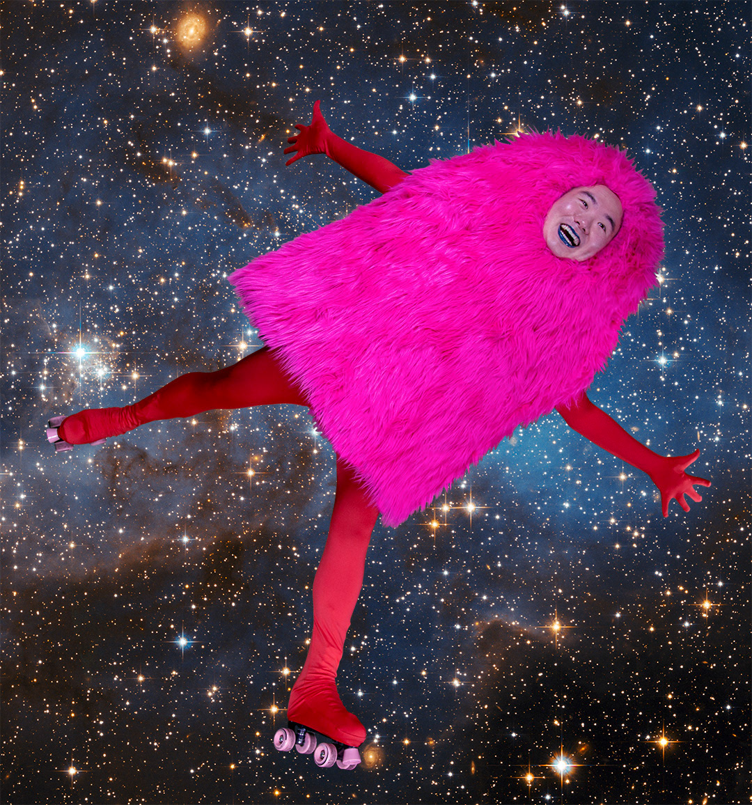 A person in wearing red tights and roller skates in a pink furry dome shaped costume flies across stars