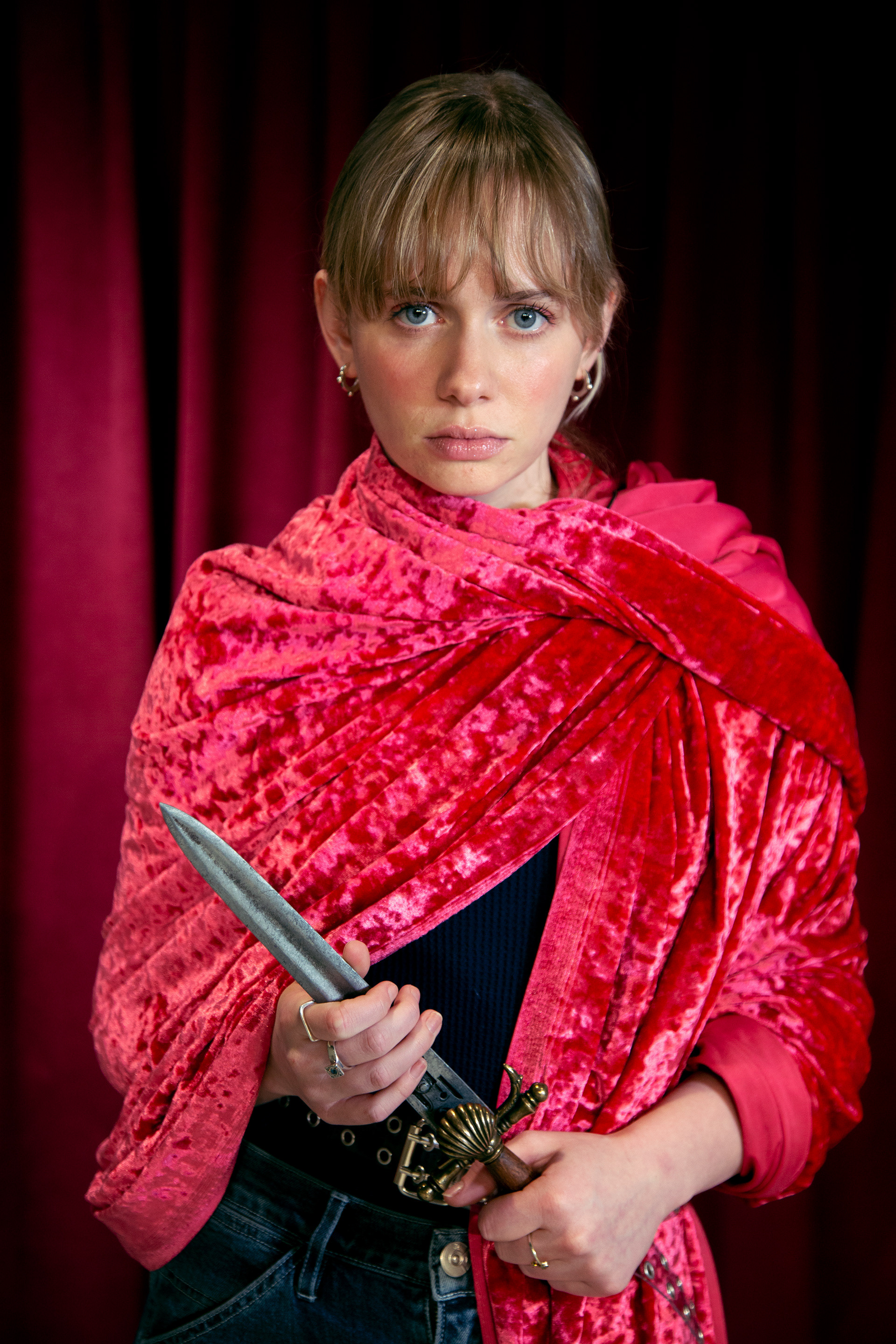 A woman stares intently wearing a red wrap holding a dagger