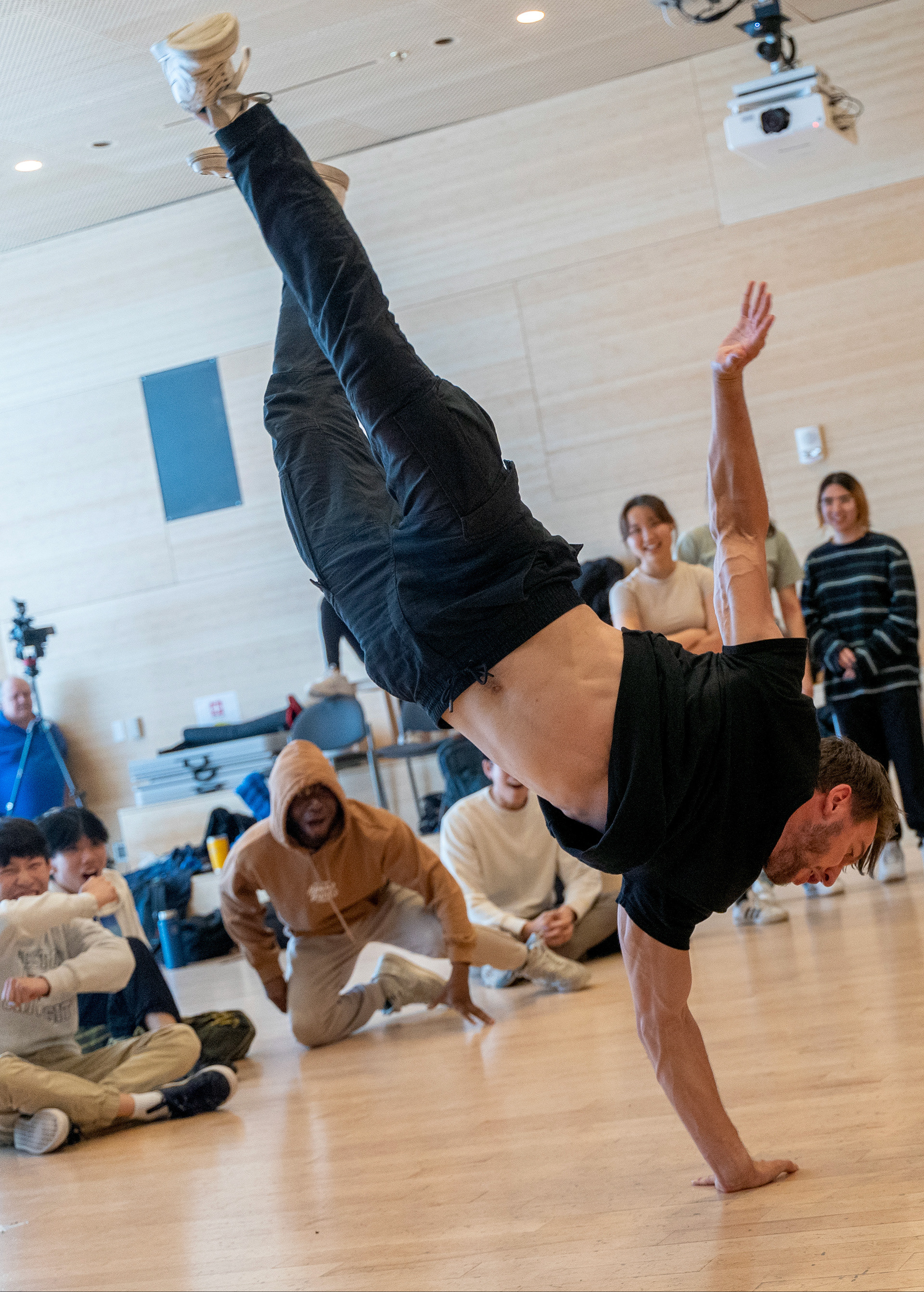 A student stands on one hand while performing breakdance move in front of cheering students