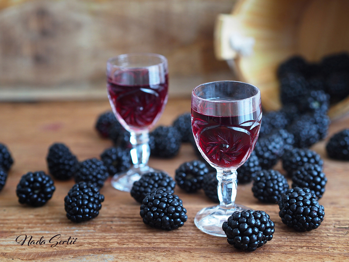 Blackberry liqueur in crystal glasses and blackberries scattered on wooden background..