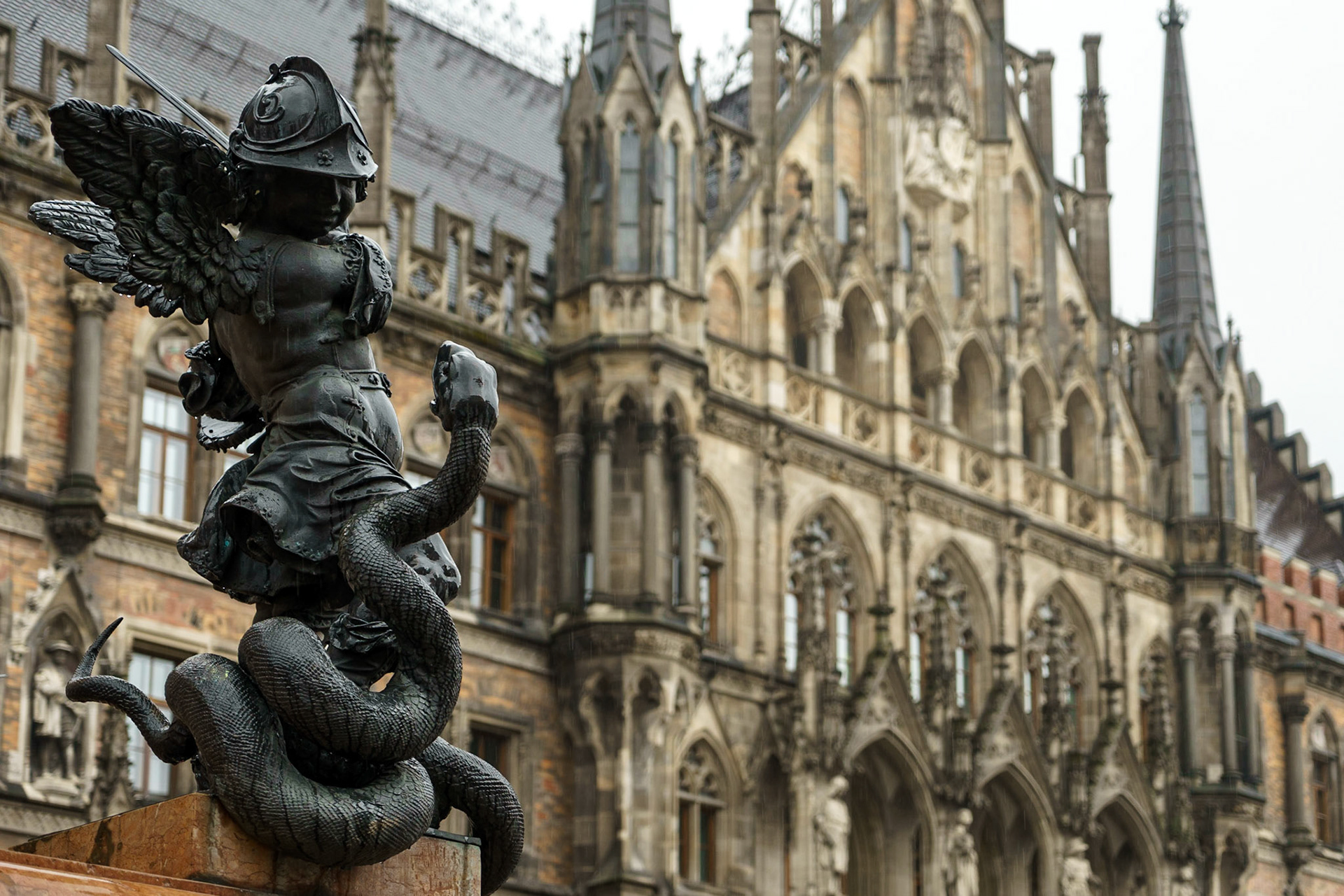 Münih Marienplatz'ın ortasında bulunan Meryem Ana Sütunu'nun çevresindeki 4 adet figürden birisi. Her bir figür, şehrin üstesinden geldiği bir zorluğu simgelemektedir - yılan, sapkınlığı temsil eder.

Arka planda ise, 1874 yılında kullanıma açılan Neues Rathaus, yani "Yeni" Belediye Sarayı görülüyor.