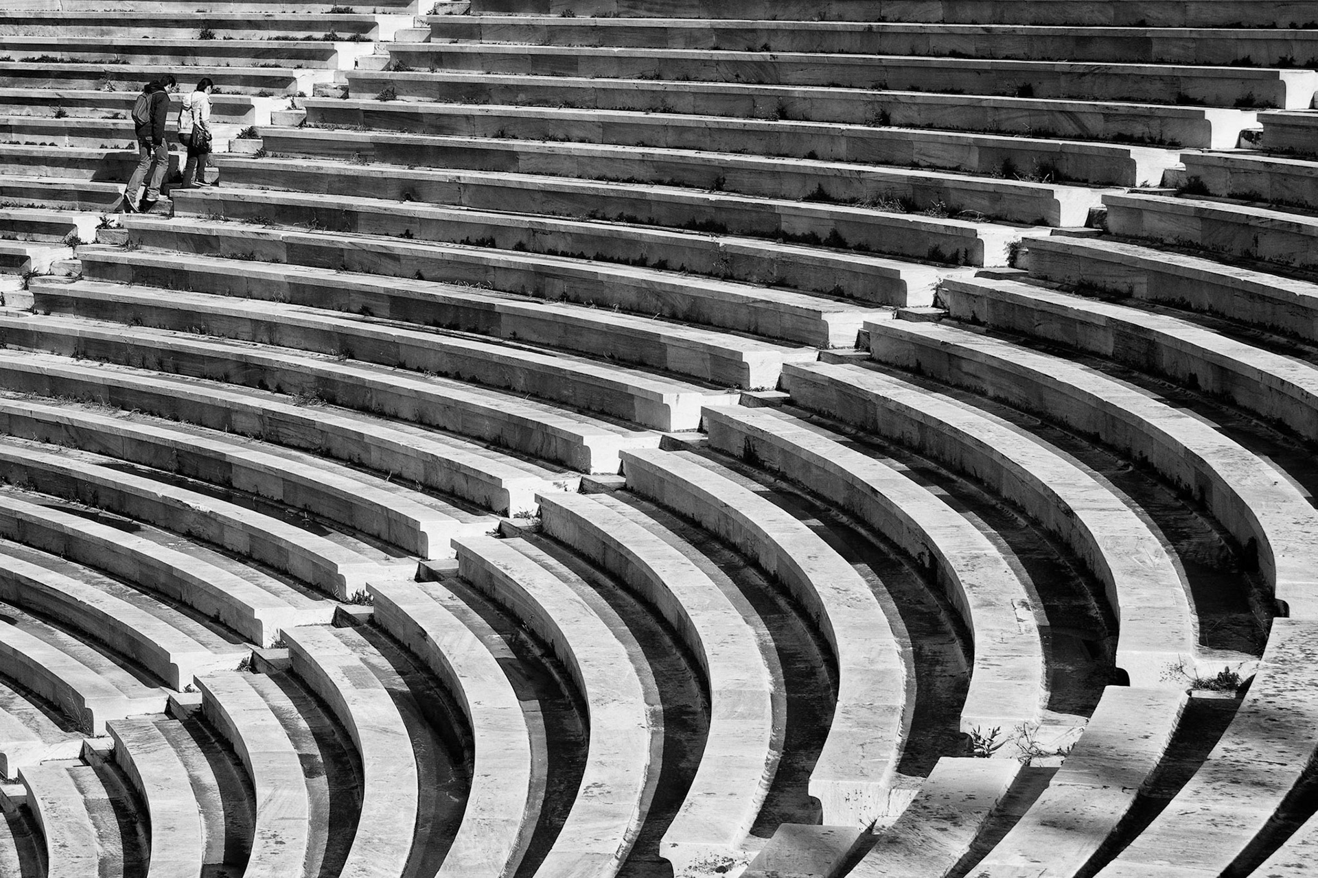 Panathenaic Stadyum'un mermer merdivenlerine güneş ışığının vurmasıyla oluşan katmanlarla birlikte, merdivenleri en tepeye kadar tırmanmaya kararlı olan bir çift.